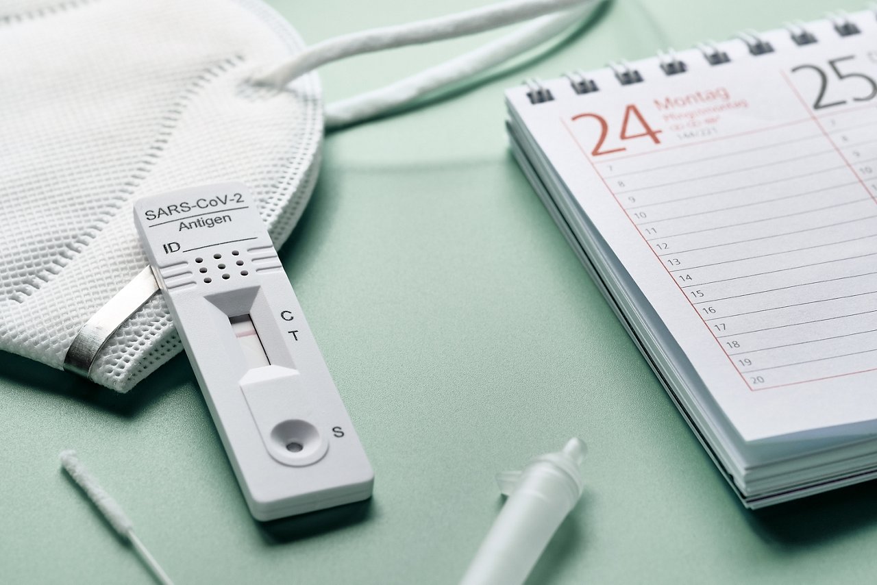 Week planner, chnelltest, rapid corona test in German language. Week planner calendar and pp2 medical face mask on green table. Test-to-go concept arrangement.