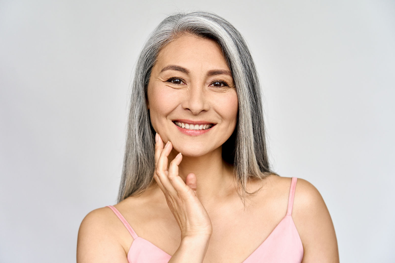 Headshot portrait of gorgeous happy middle aged mature asian woman, senior older 50 year lady looking at camera touching her face isolated on white. Ads of lifting anti wrinkle skin care, spa.