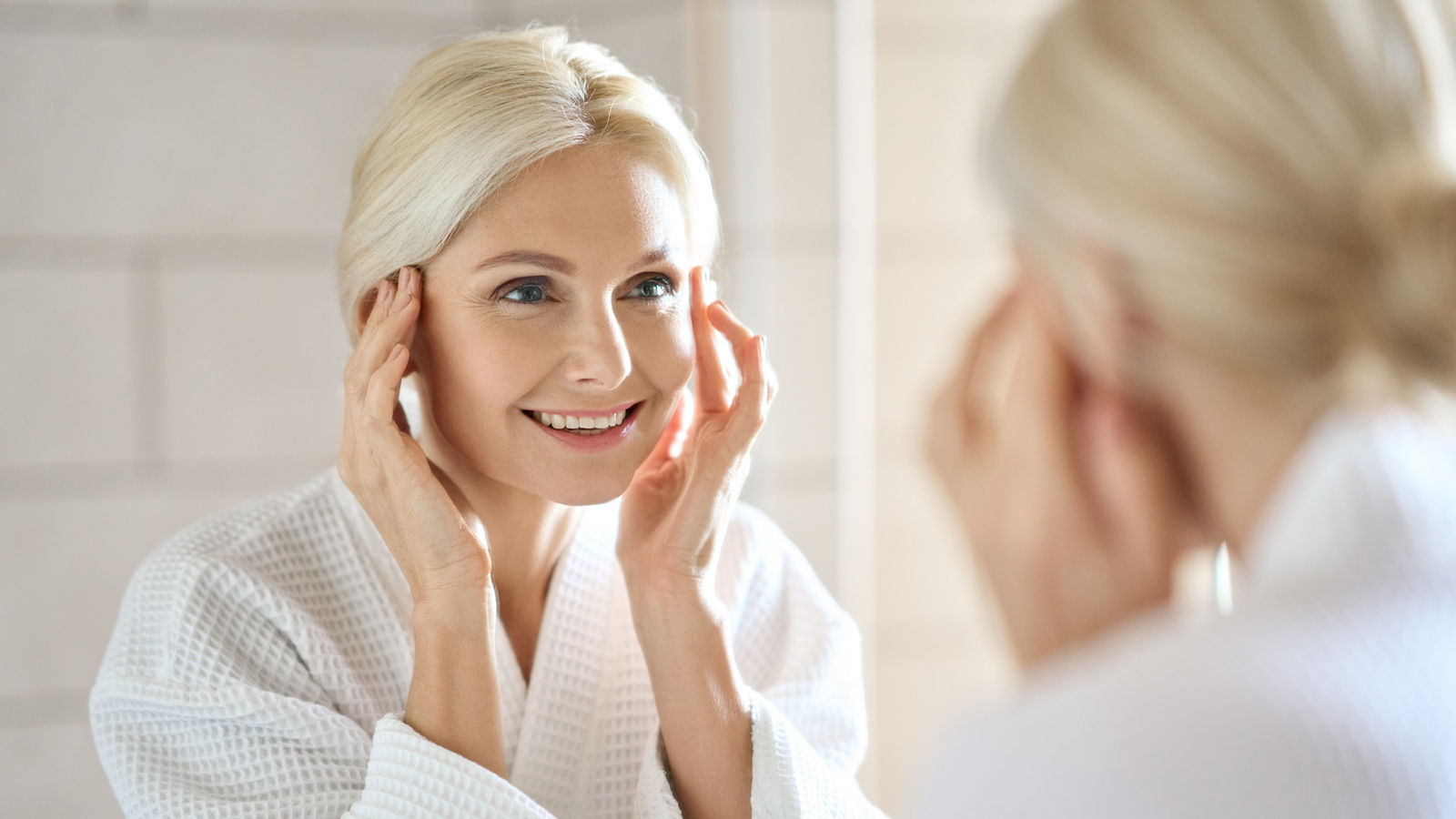 Attractive mid age woman smiling looking at mirror. Skincare concept.