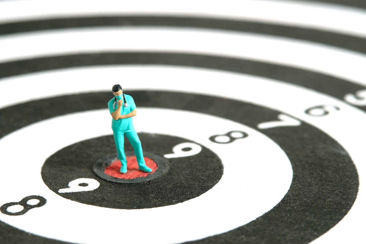 Miniature people toy figure photography. A men doctor or nurse thinking in the middle dartboard target. Image photo