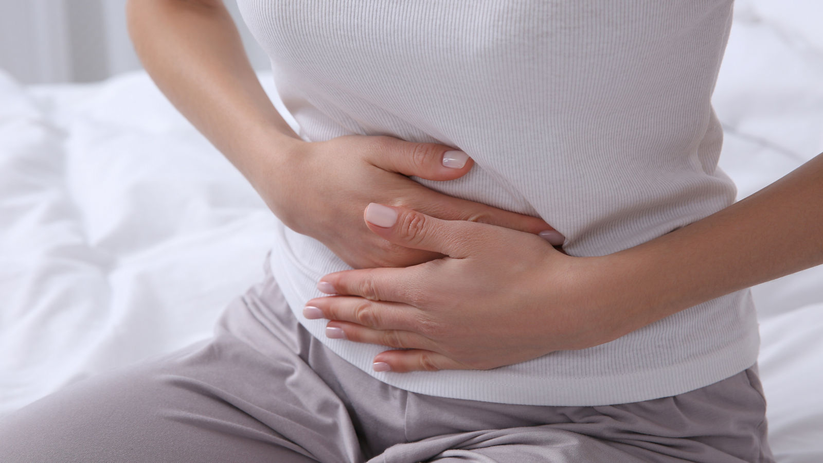 Young woman suffering from stomach ache on bed, closeup