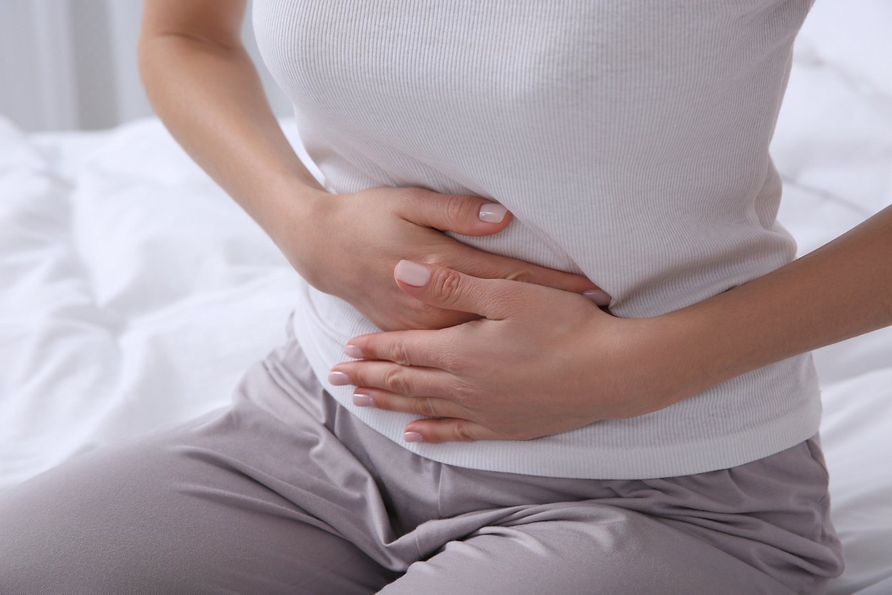 Young woman suffering from stomach ache on bed, closeup