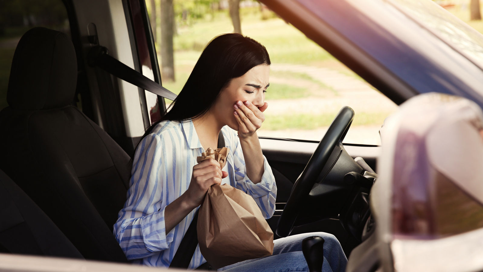 Young woman with paper bag suffering from nausea in car