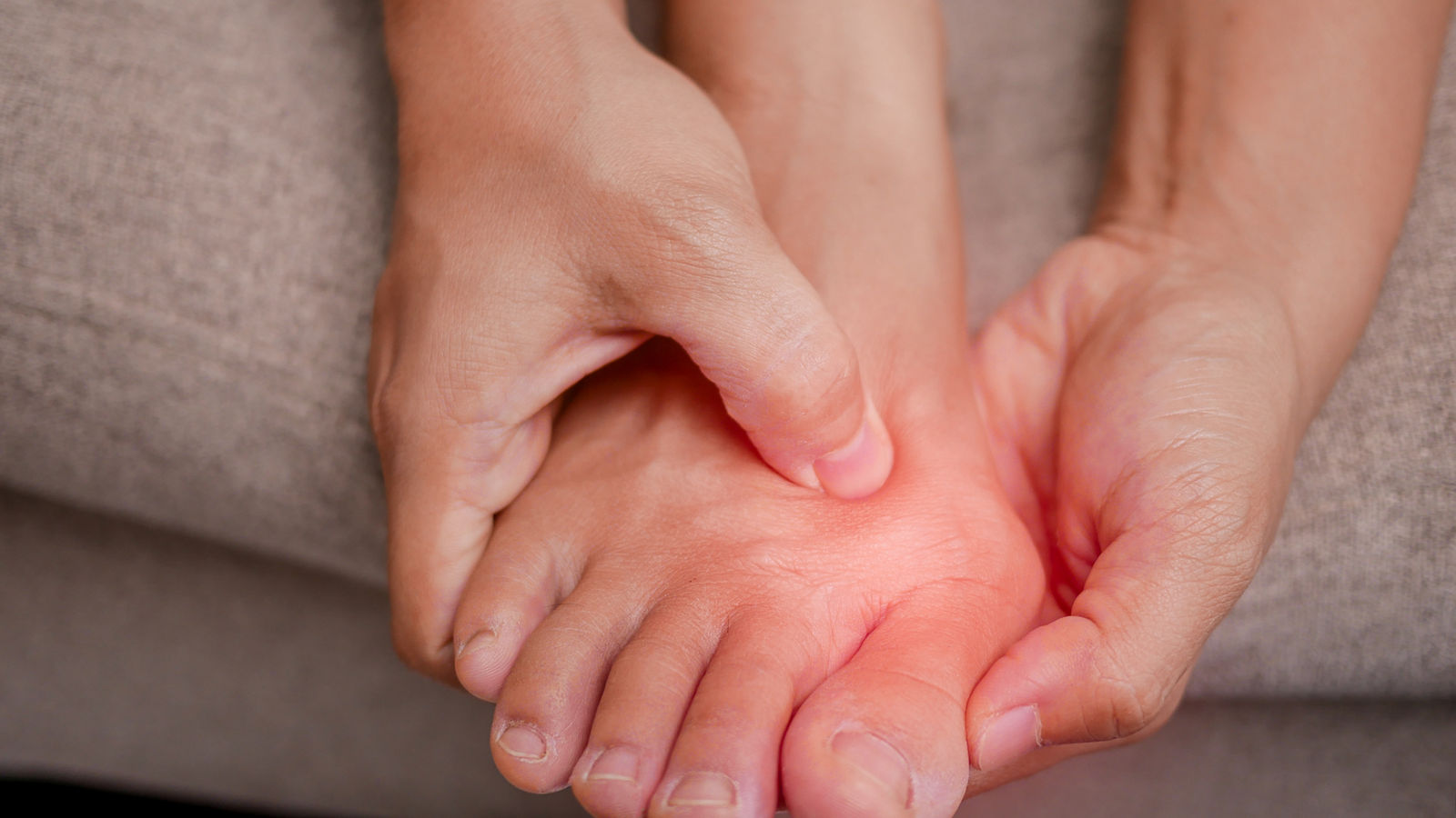 Closeup of female holding her painful feet and massaging her bunion toes to relieve pain. Swollen bunion at the edge of the big toe causes deformity (Hallux valgus). Woman's health concept.