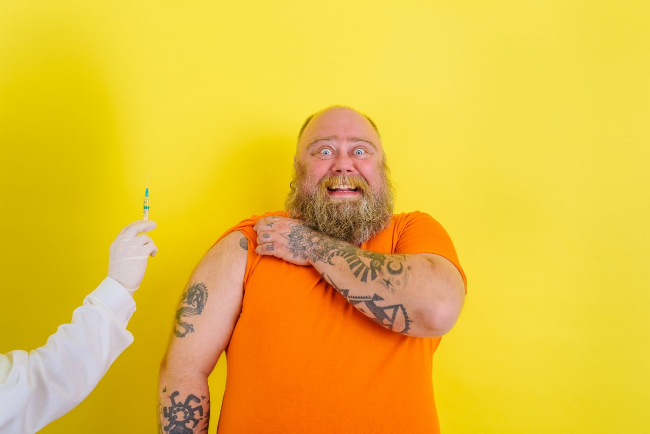 Ein tätowierter Mann mit Bart hat Angst vor der nahenden Impfspritze 