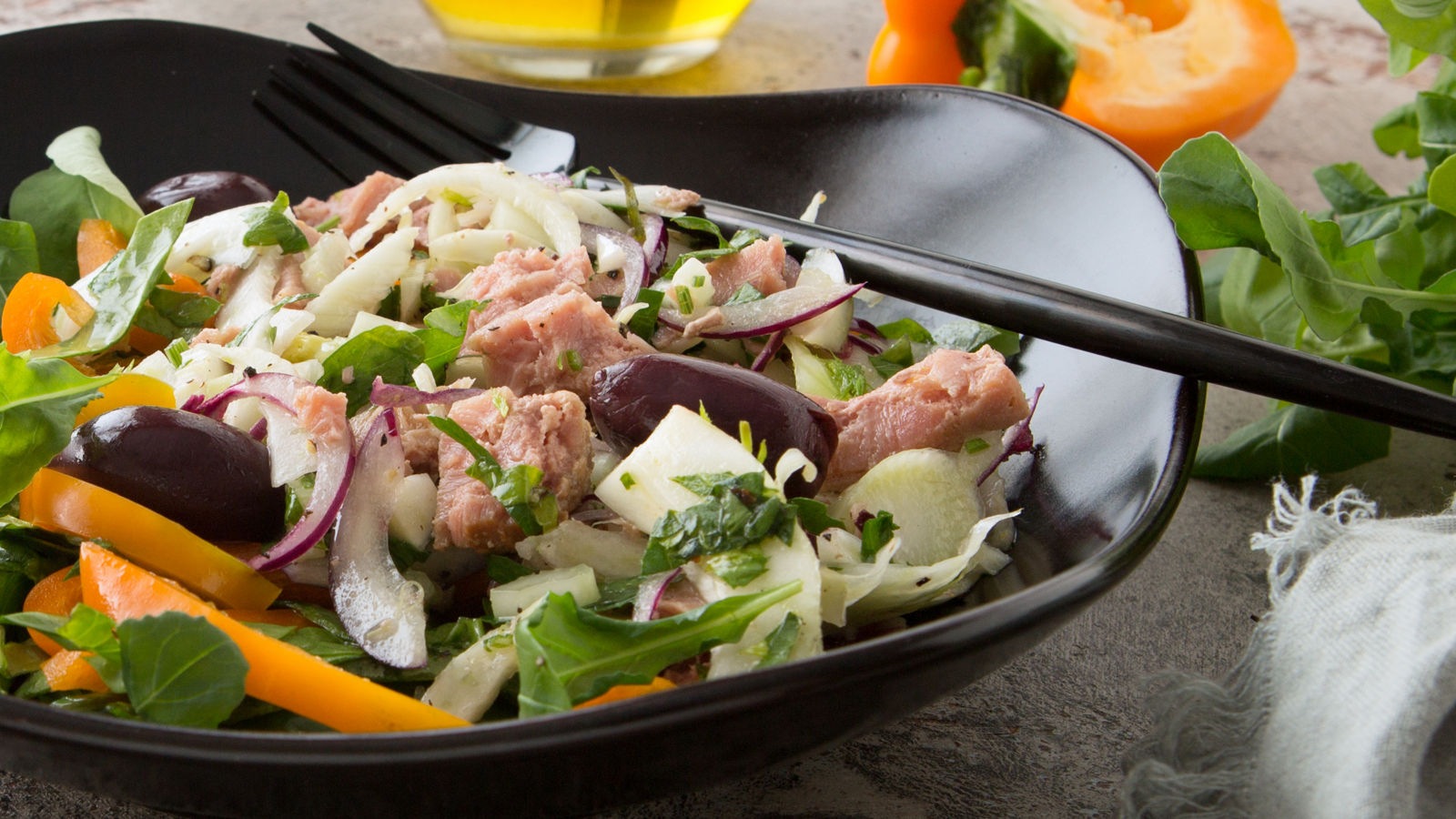 a plate of tuscan salad with tuna, fennel, peppers and olives on the table