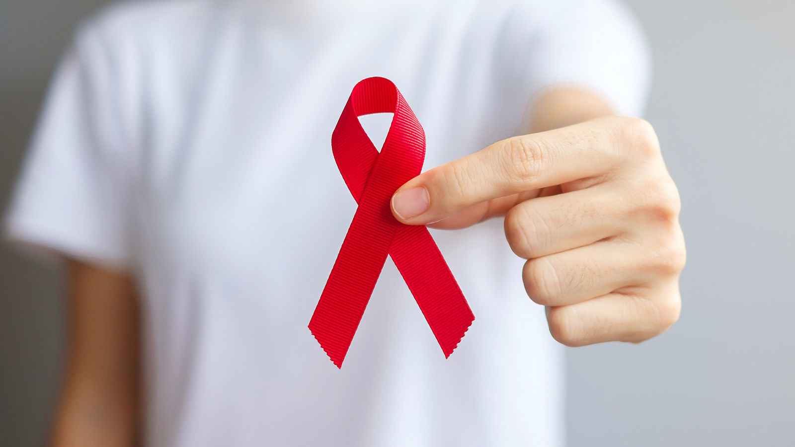 Hand holding Red Ribbon for December World Aids Day (acquired immune deficiency syndrome), multiple myeloma Cancer Awareness month and National Red ribbon week. Healthcare and world cancer day concept