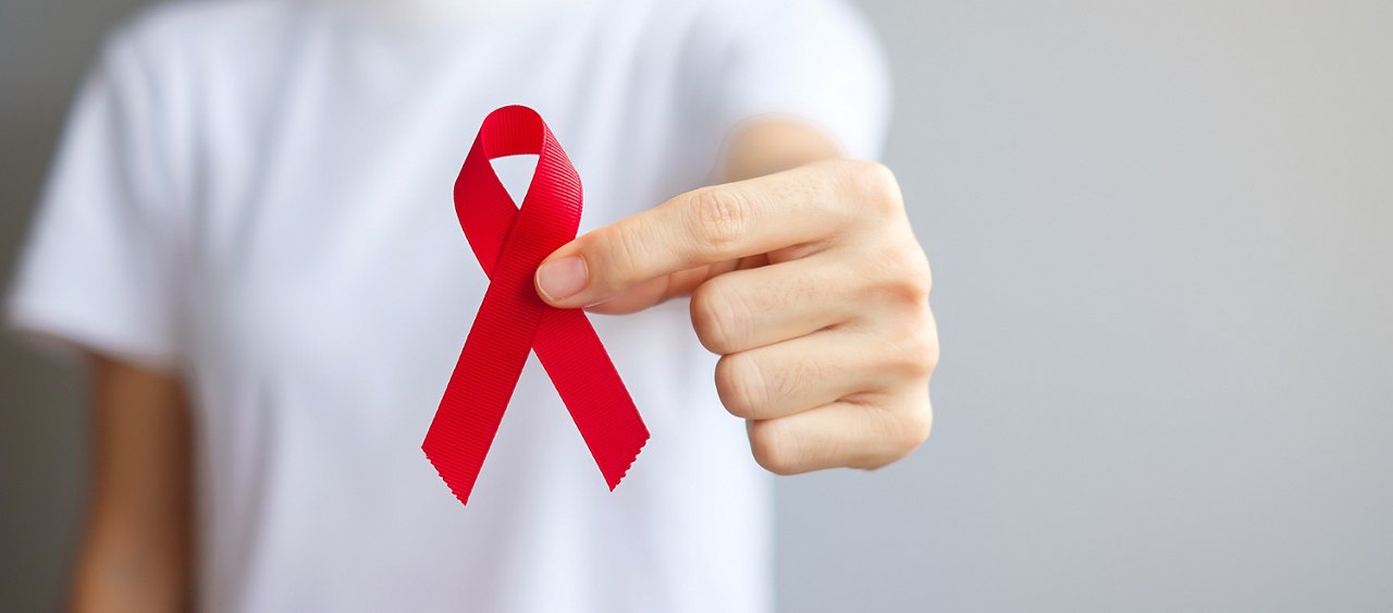 Hand holding Red Ribbon for December World Aids Day (acquired immune deficiency syndrome), multiple myeloma Cancer Awareness month and National Red ribbon week. Healthcare and world cancer day concept