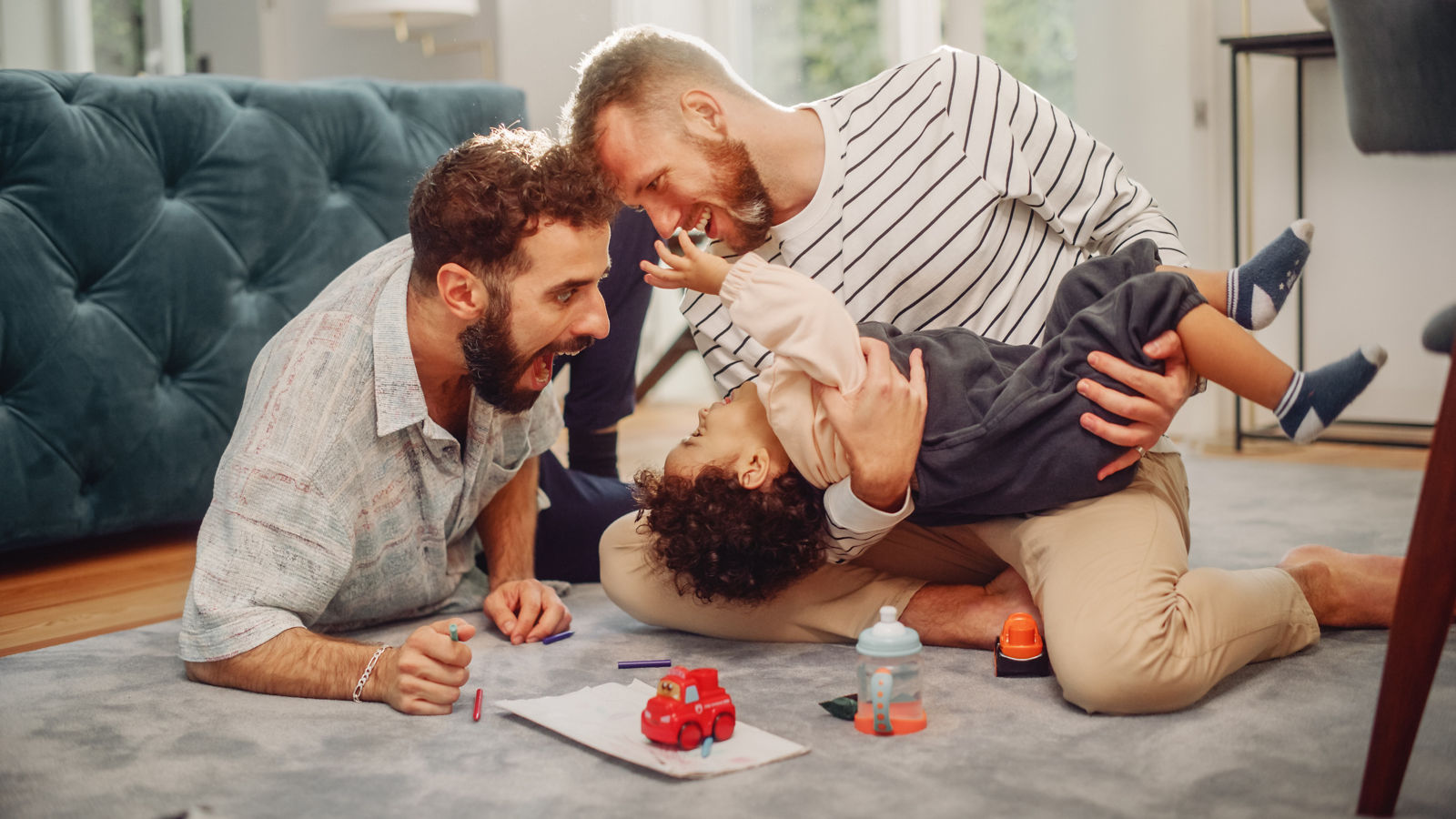 Loving LGBTQ Family Playing with Toys with Adorable Baby Boy at Home on Living Room Floor. Cheerful Gay Couple Nurturing a Child. Concept of Diverse Childhood, New Life, Parenthood.