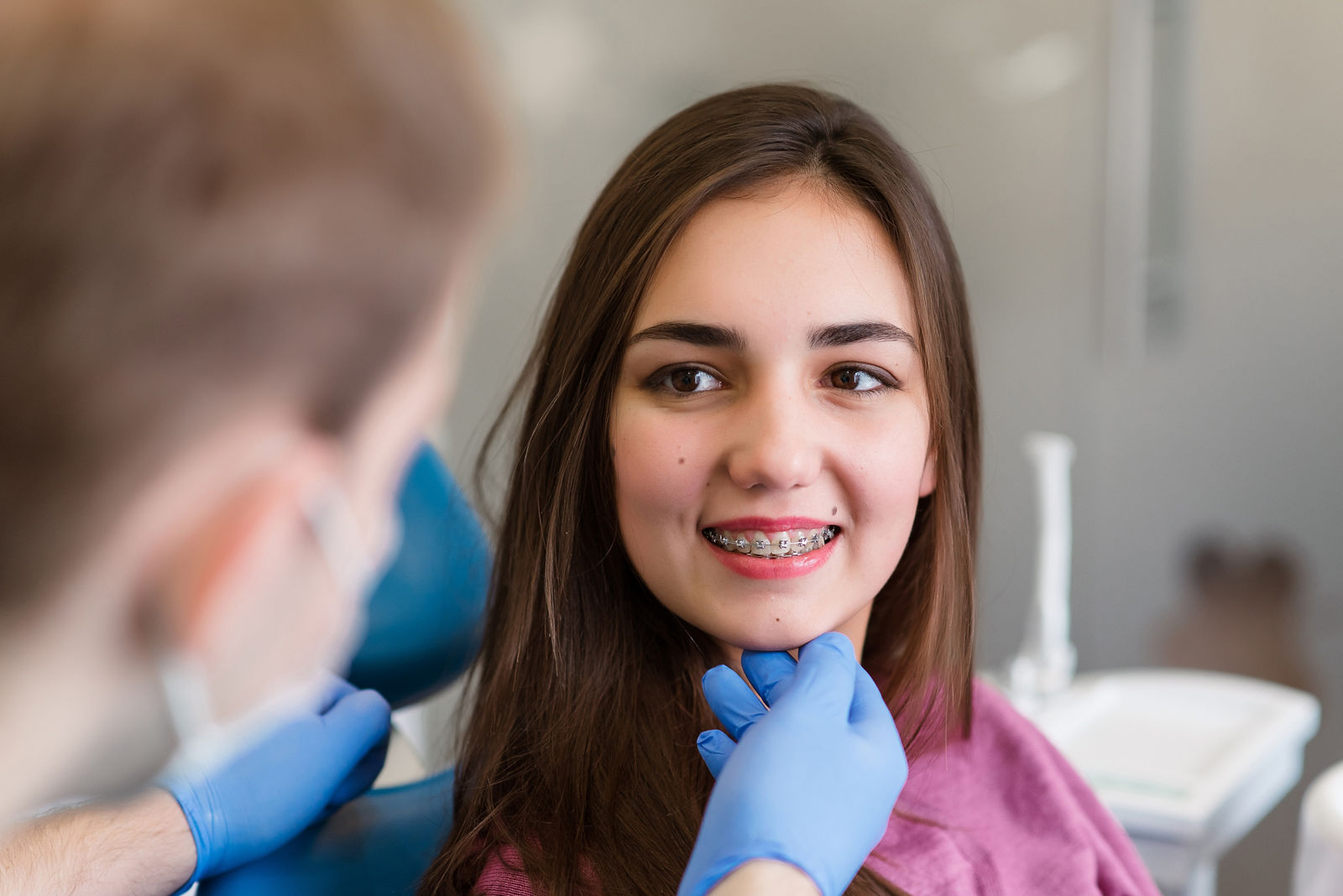 Nahaufnahme einer Frau mit Brackets, die in einer Klinik eine Zahnspange erhält. Kieferorthopäde benutzt Zahnspiegel und Zange beim Anbringen der Zahnspange an den Zähnen der Patientin. Konzept der Zahnmedizin.