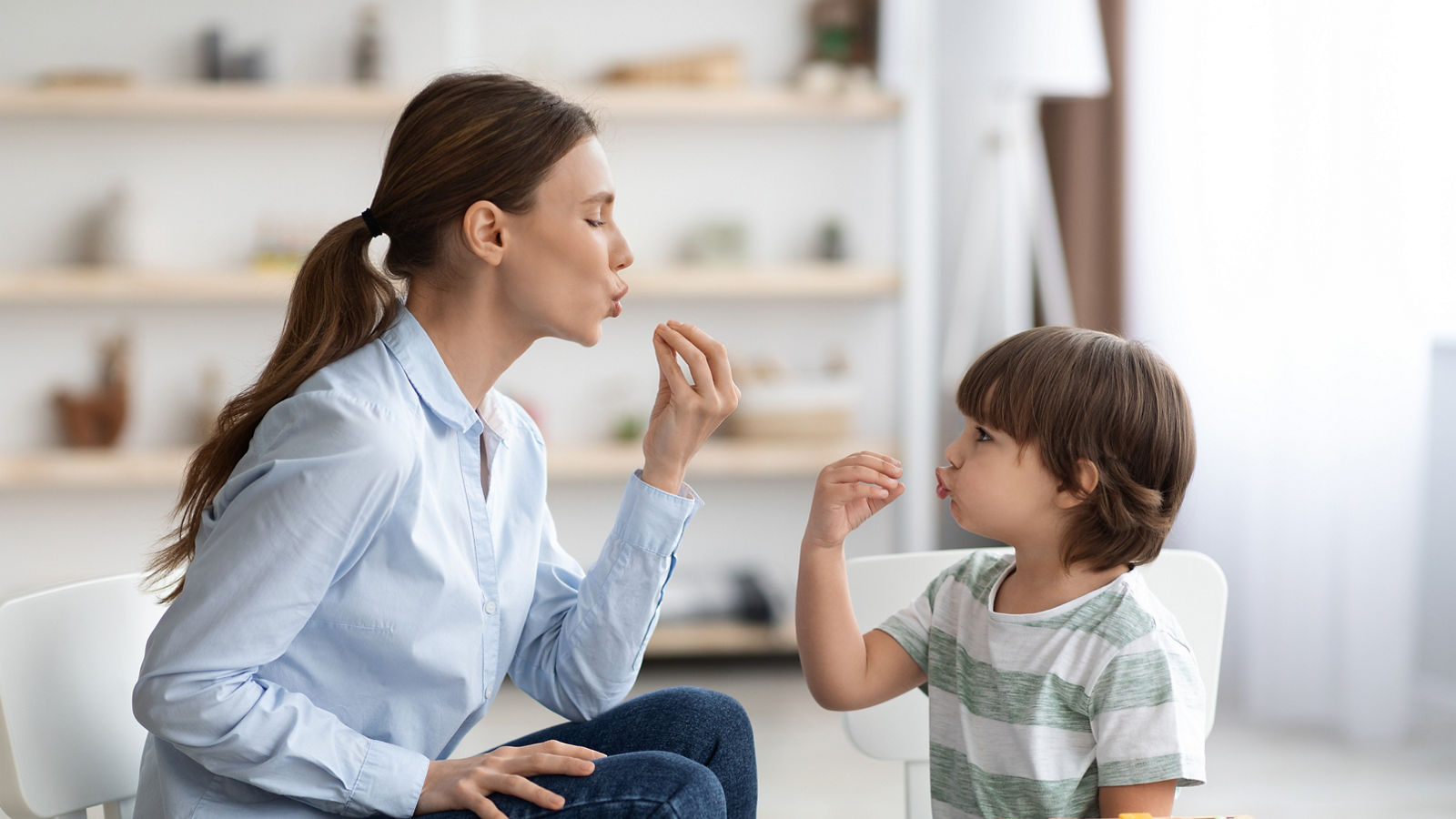 Young woman speech therapist studying together with small kid, learning practice pronunciation exercises with little boy