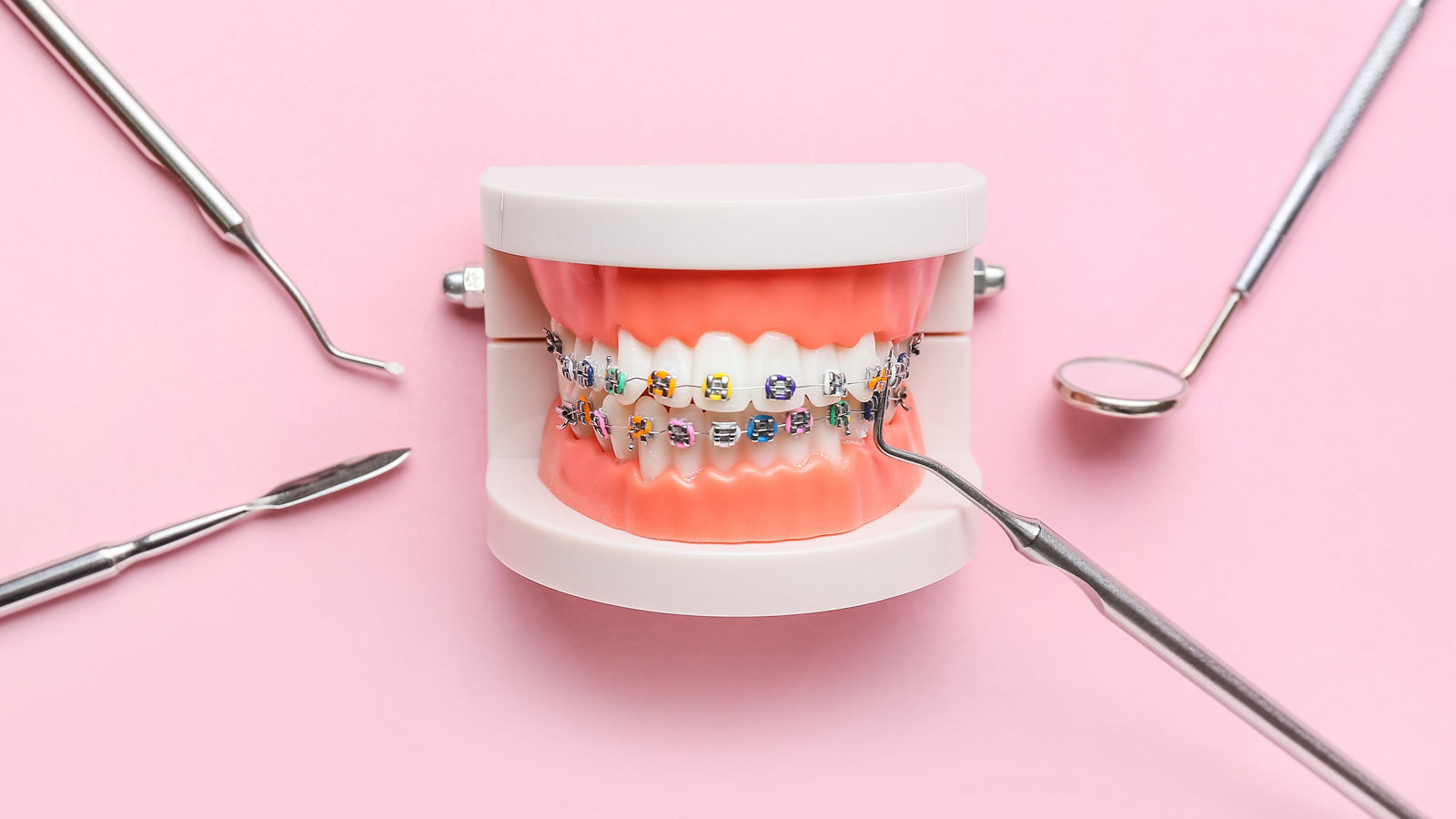 Model of jaw with dental braces and dentist tools on pink background