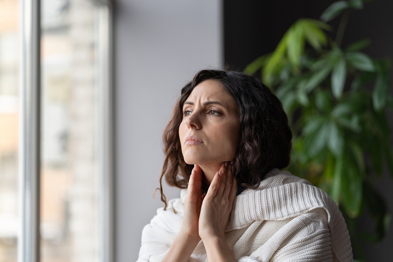 Young sick unhealthy woman covered in knitted plaid suffering from sore throat and swollen glands, feeling discomfort and pain when swallowing. Tonsillitis, laryngitis and lymph node inflammation