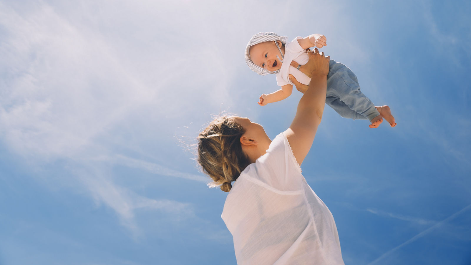 Mother throwing baby up against the blue sky. Happy family outdoors. Mom and baby at summer on nature. Positive human emotions and feelings.