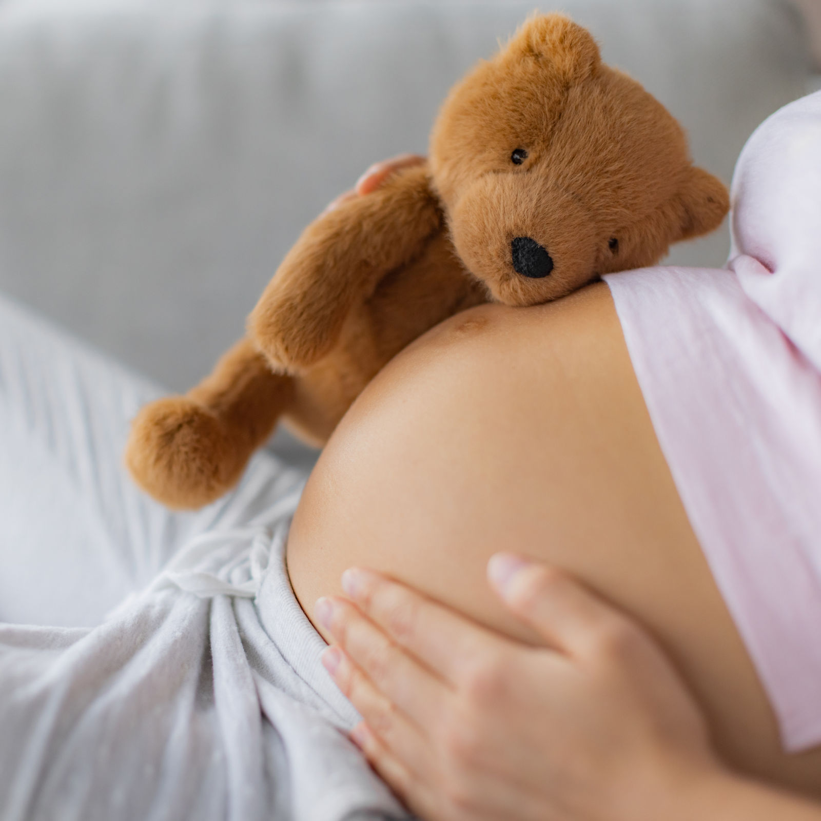 Pregnant woman caressing belly hugging teddy bear baby toy on pregnancy bump waiting for the birth of her child.