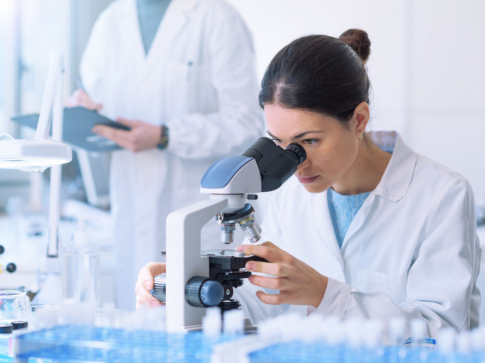 Students working in the clinical laboratory, a researcher is using a microscope in the foreground, scientific research concept