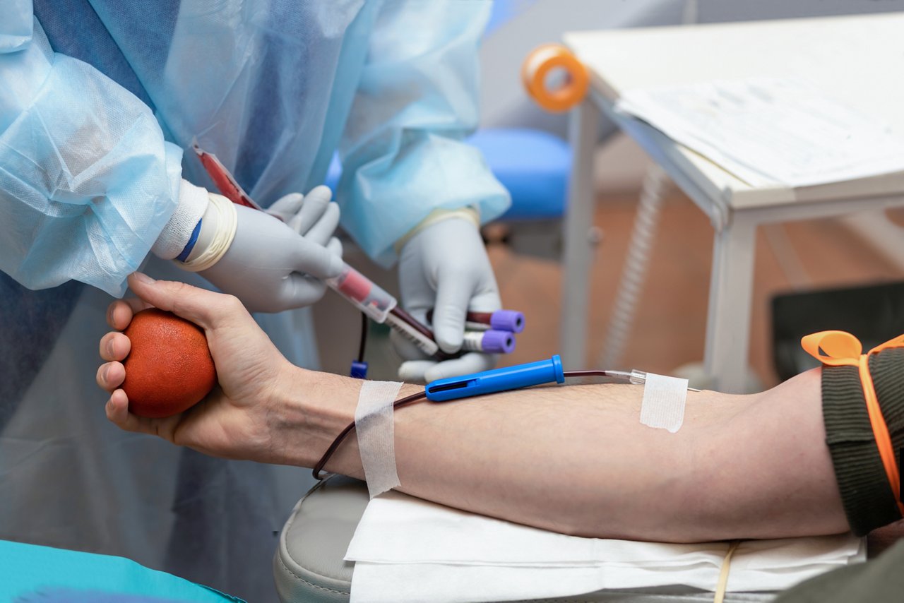 bone marrow donation. male hand holding red ball, man with blood transfusion system, blood bag. soft focus