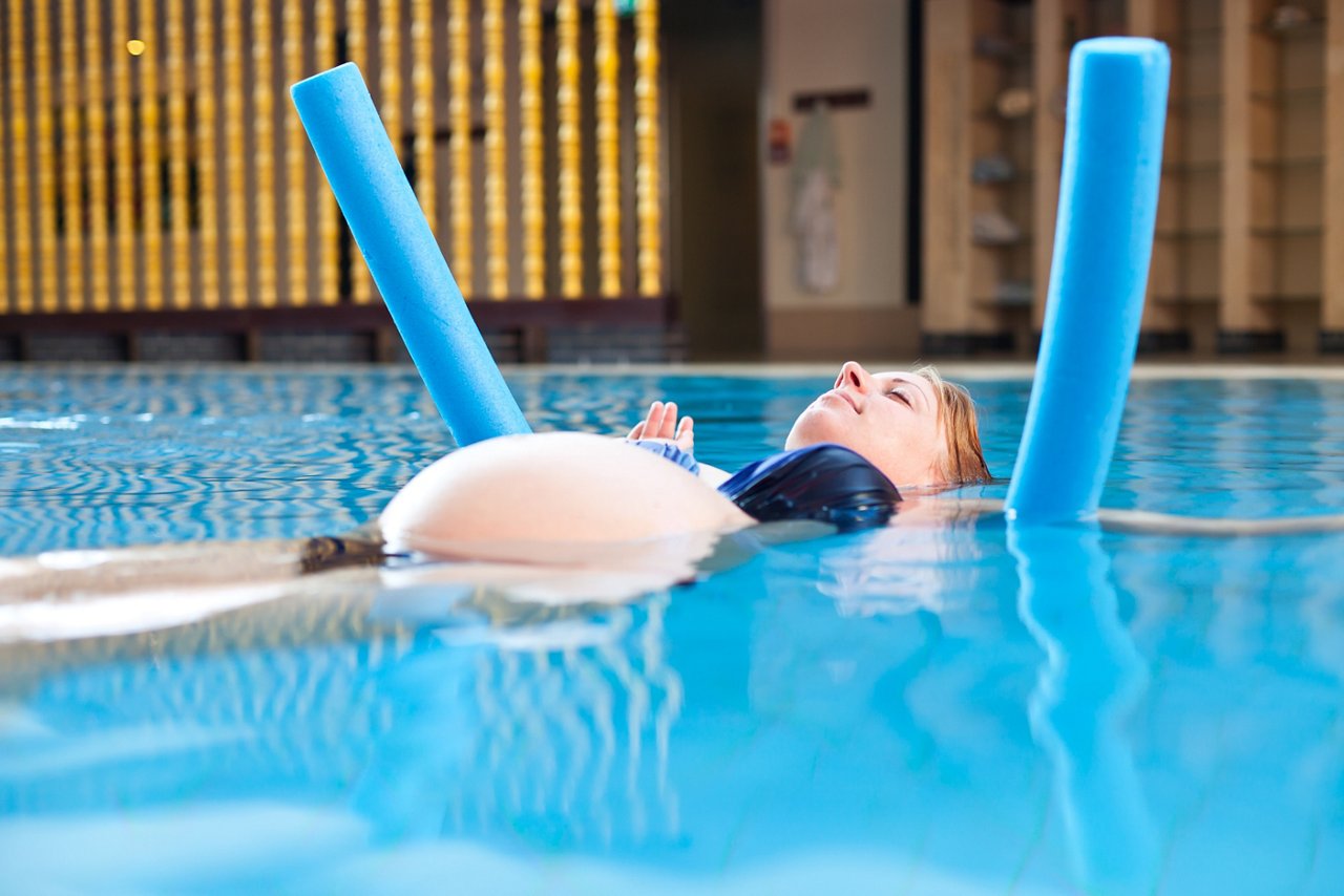 Schwangere Frau Bei Wassergymnastik in einem Schwimmbad mit einer Poolnudel