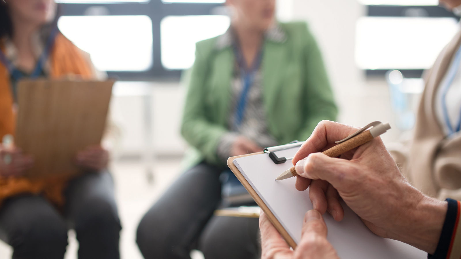 Elderly people attending group therapy session at nursing house, sitting in circle, having conversation with psychologist, close-up