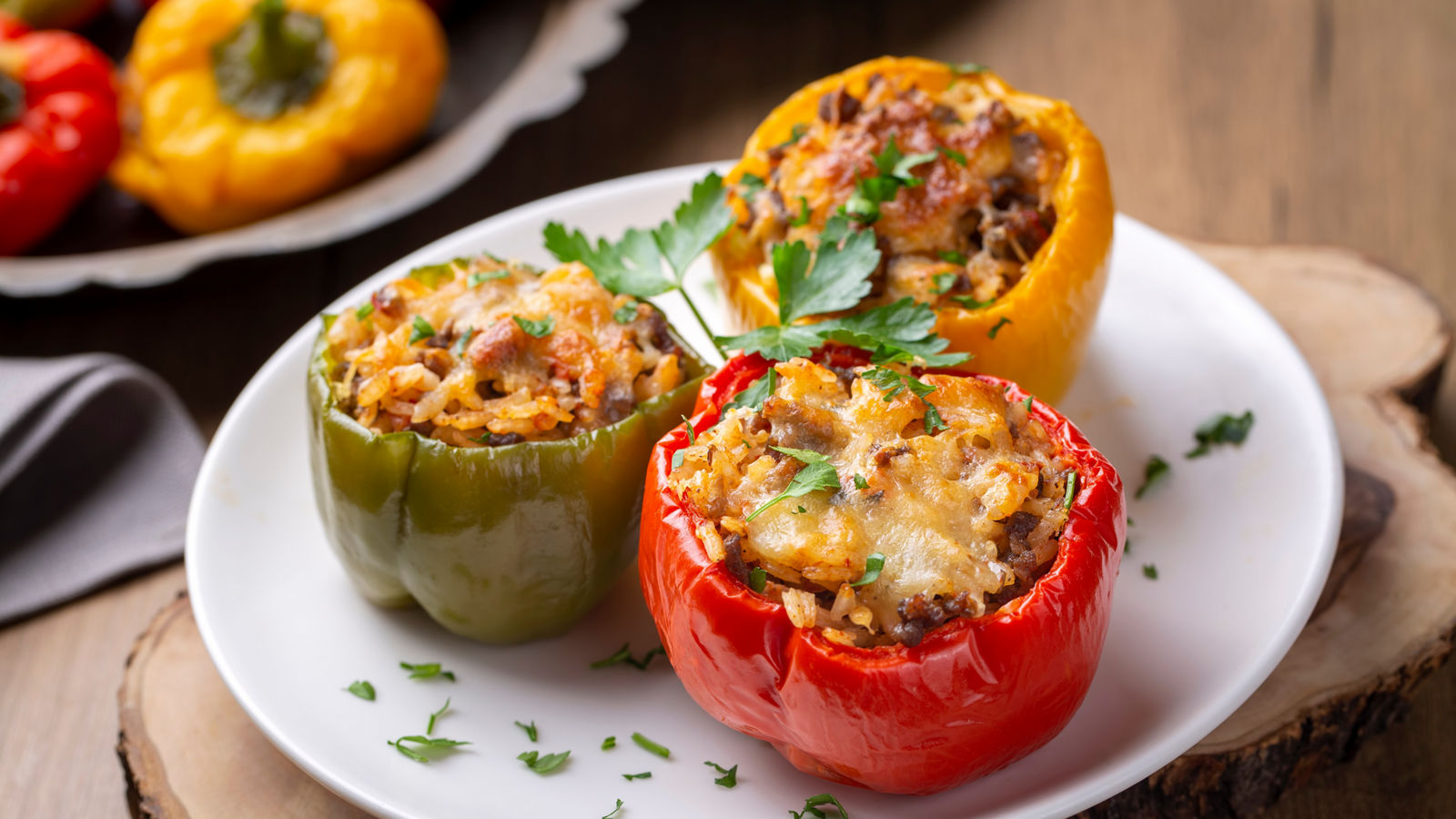 Stuffed peppers, halves of peppers stuffed with rice, dried tomatoes, herbs and cheese in a baking dish on a blue wooden table, top view. (Turkish name; biber dolmasi)