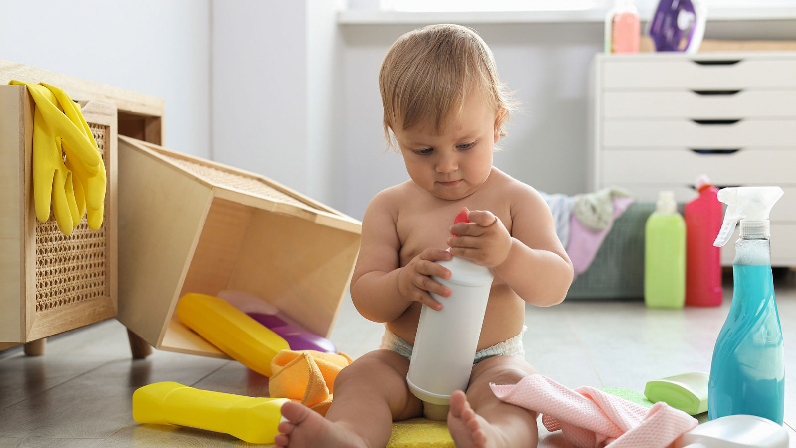 Cute baby playing with bottle of detergent on floor at home. Dangerous situation