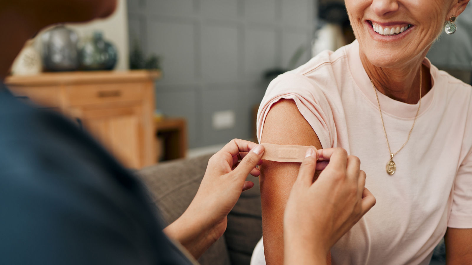 Woman, smile and plaster after injection for vaccine against covid. Happy, senior and lady vaccination for coronavirus on sofa in doctor office for health, wellness and safety from global pandemic