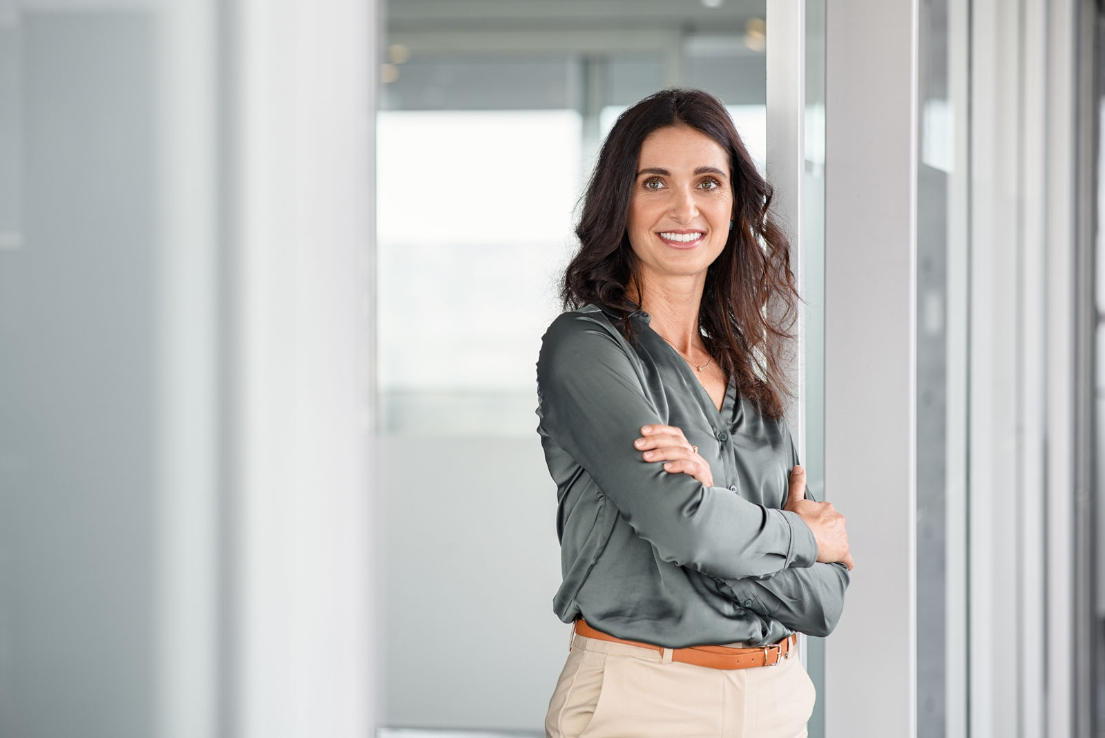 Portrait of mature business woman with arms crossed looking at camera. Happy smiling mid businesswoman standing in modern office with copy space. Confident latin woman in formalwear standing in workplace.