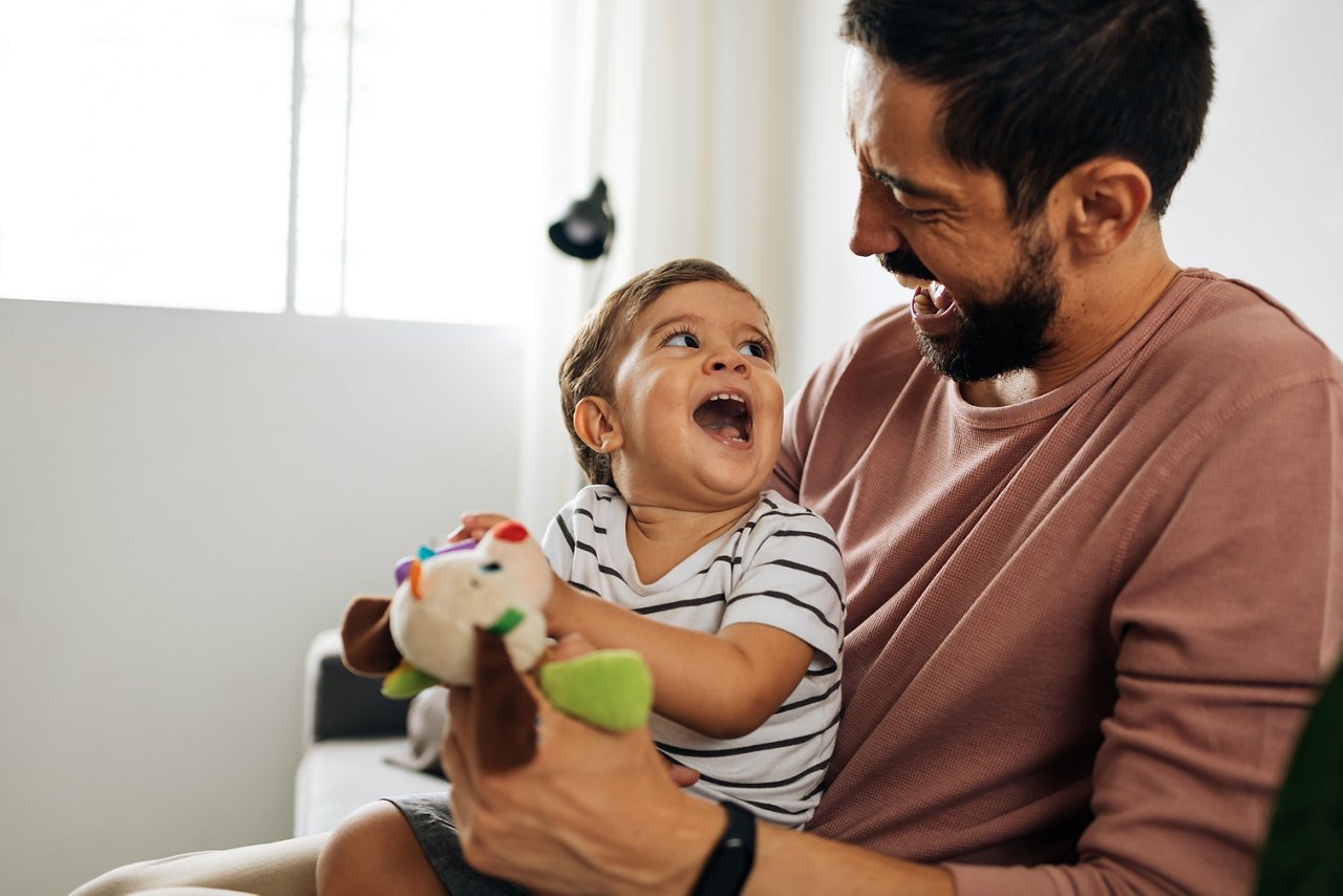 Father and baby son with teddy bear at home. Candid moment of father and son together.