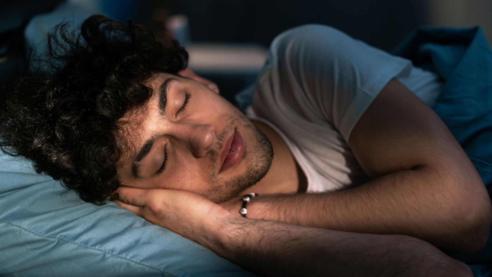 Handsome young man sleeping on pillow in dark room at night, resting at night time. Healthy sleep