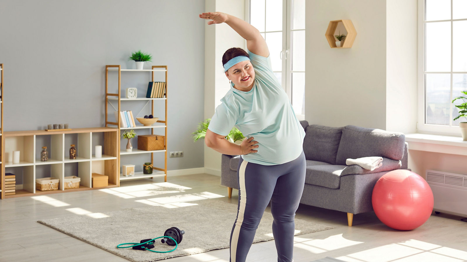 Funny fat smiling girl wearing sportswear doing sport fit exercise at home.