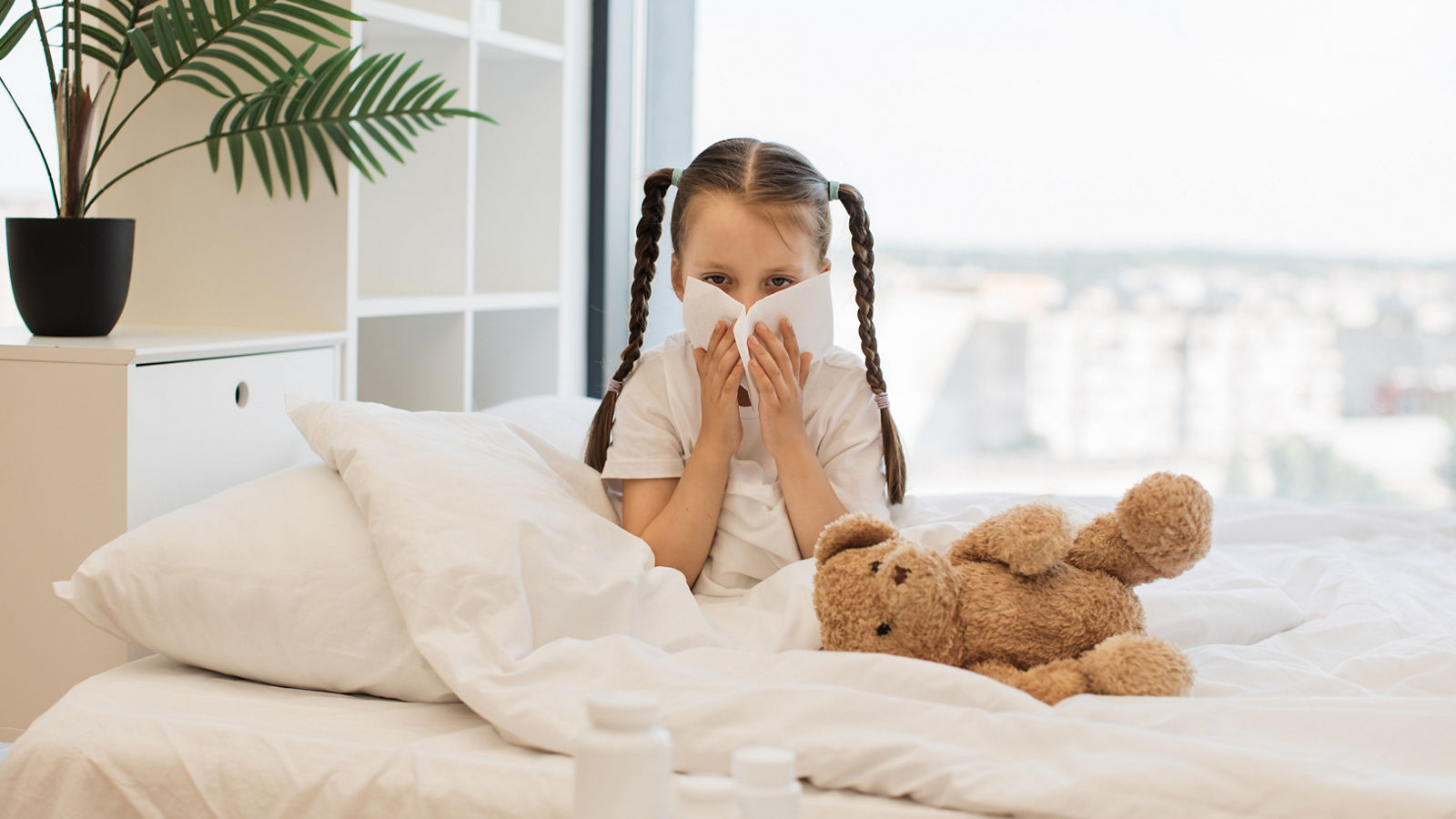 Mädchen mit Erkältung sitzt im Bett mit Teddy