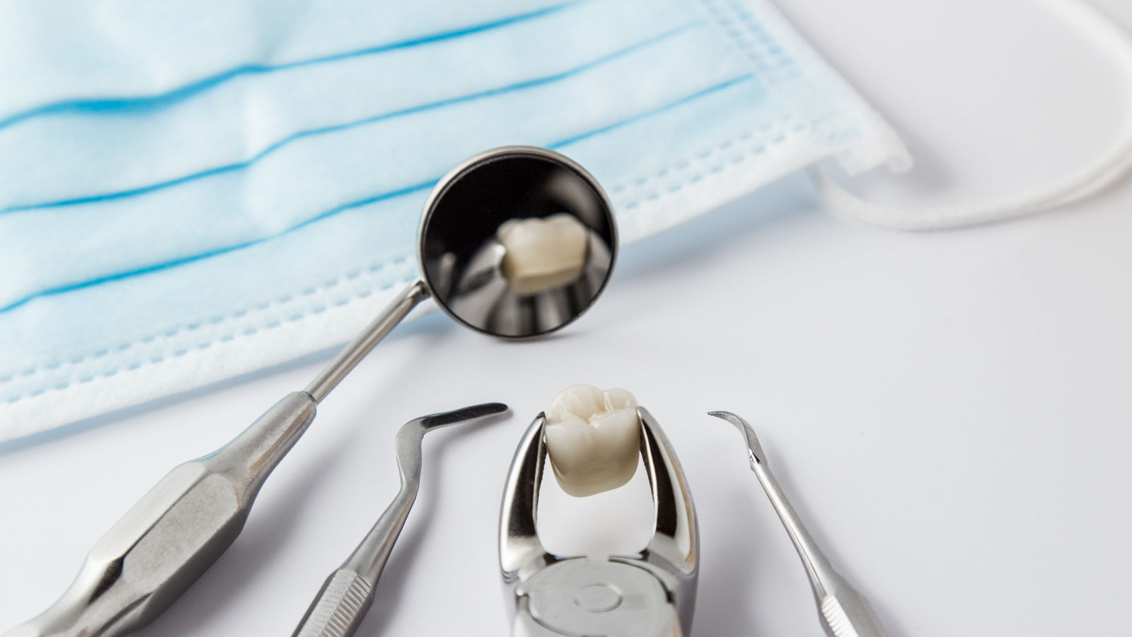 Zahnextraktion Konzept mit einem Array aus Edelstahl Dentalwerkzeuge und eine Maske mit dem extrahierten Zahnes in den Zangen verschränkt und in den Spiegel reflektierten