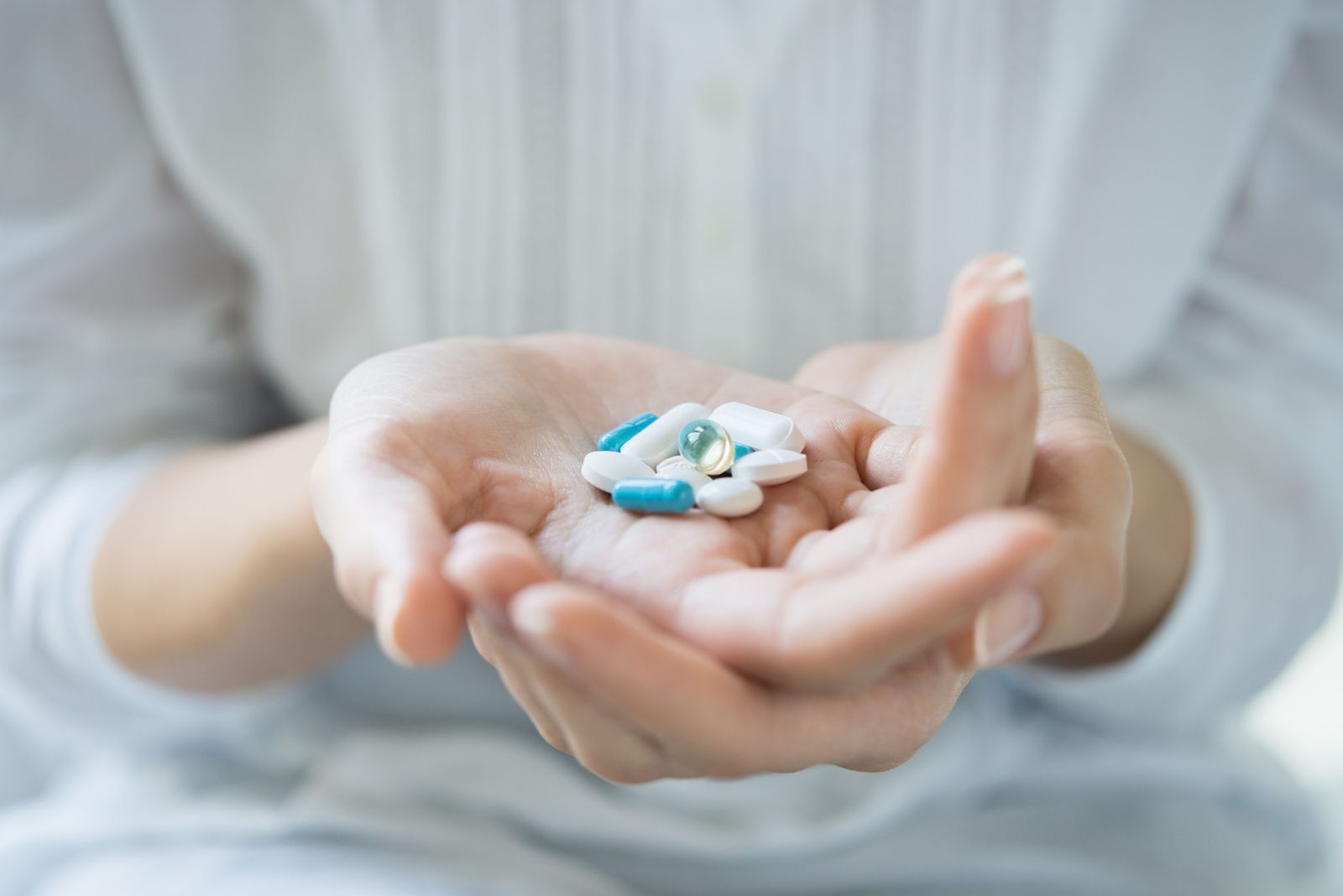 Closeup shot of a woman holding various pills on hand. Girl with white shirt showing medicines and pills indoor. Shallow depth of field with focus on pill. 
