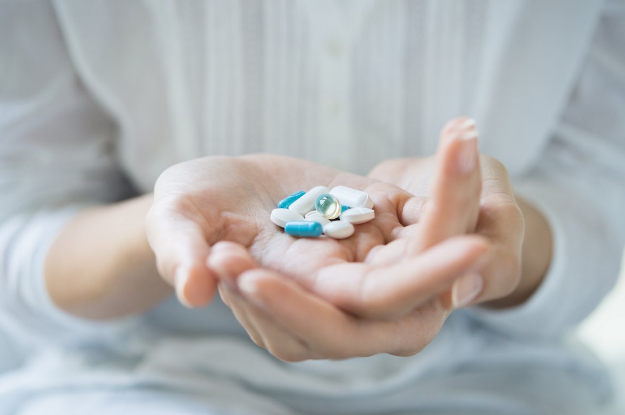 Closeup shot of a woman holding various pills on hand. Girl with white shirt showing medicines and pills indoor. Shallow depth of field with focus on pill. 
