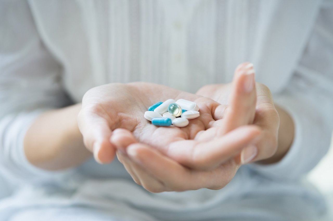 Hände einer Frau halten eine Vielzahl unterschiedlicher Pillen, Kapseln und Tabletten