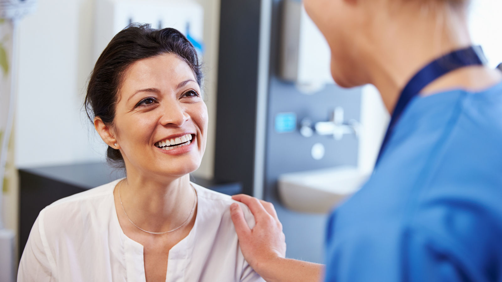Female Patient Being Reassured By Doctor In Hospital Room