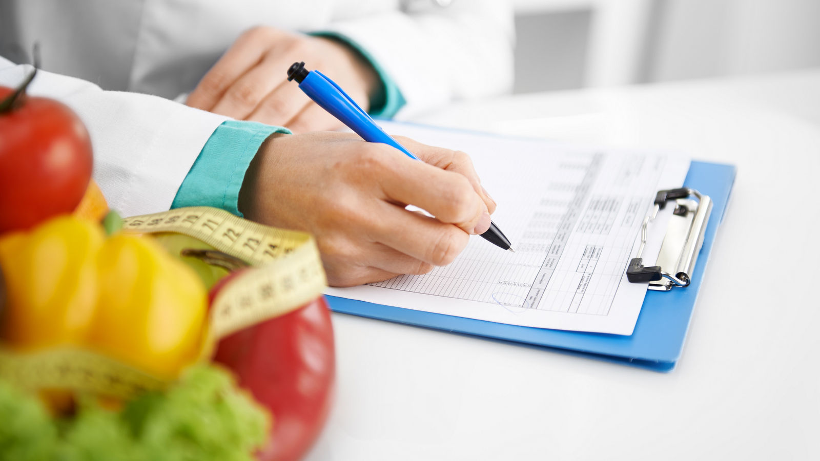 Arzt verschreibt Rezept auf Block mit Obstkorb und Maßband an der Seite gegen Adipositas