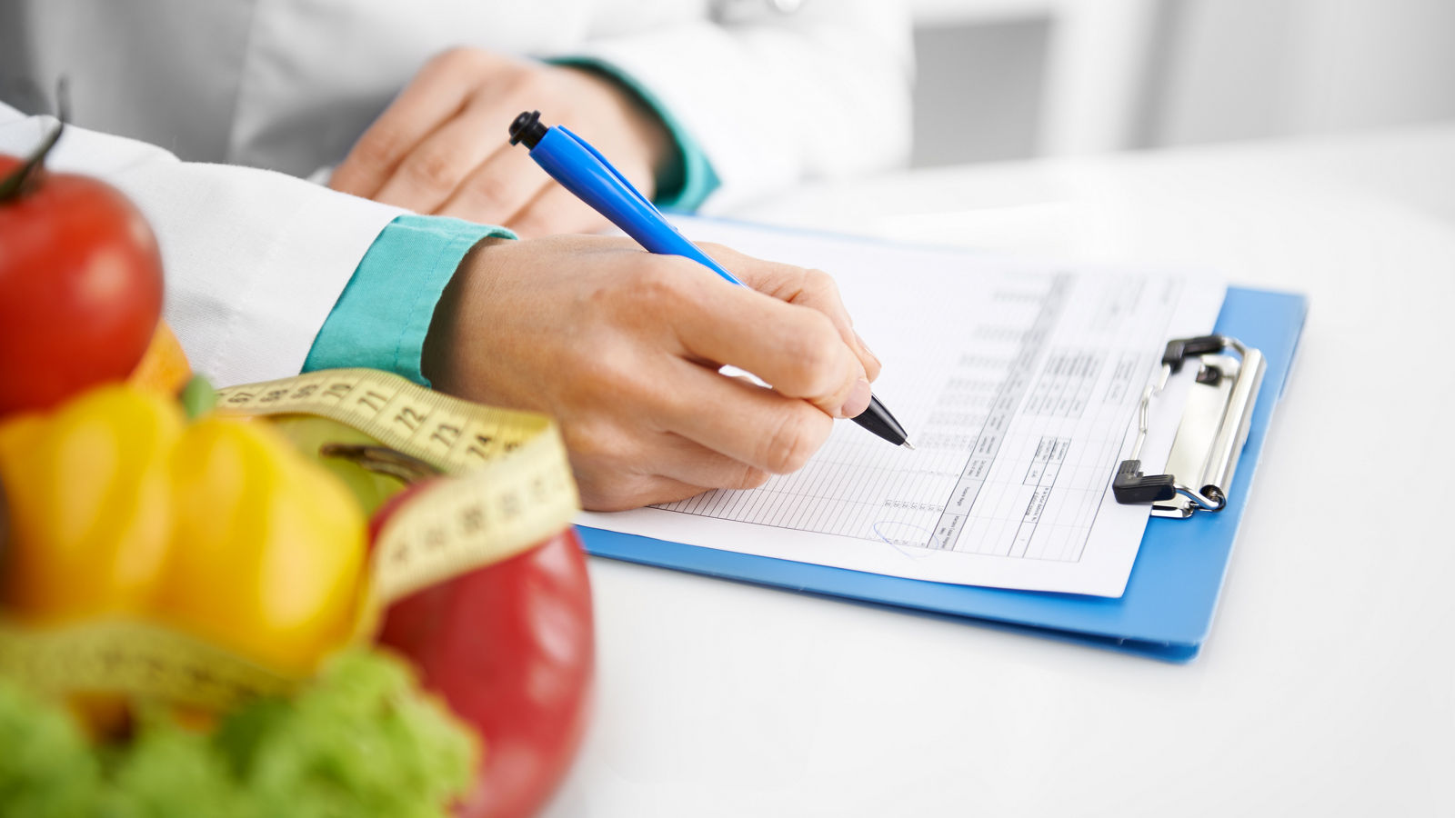 Doctor nutritionist writing case history in the office. Young woman dietitian prescribing recipe. 