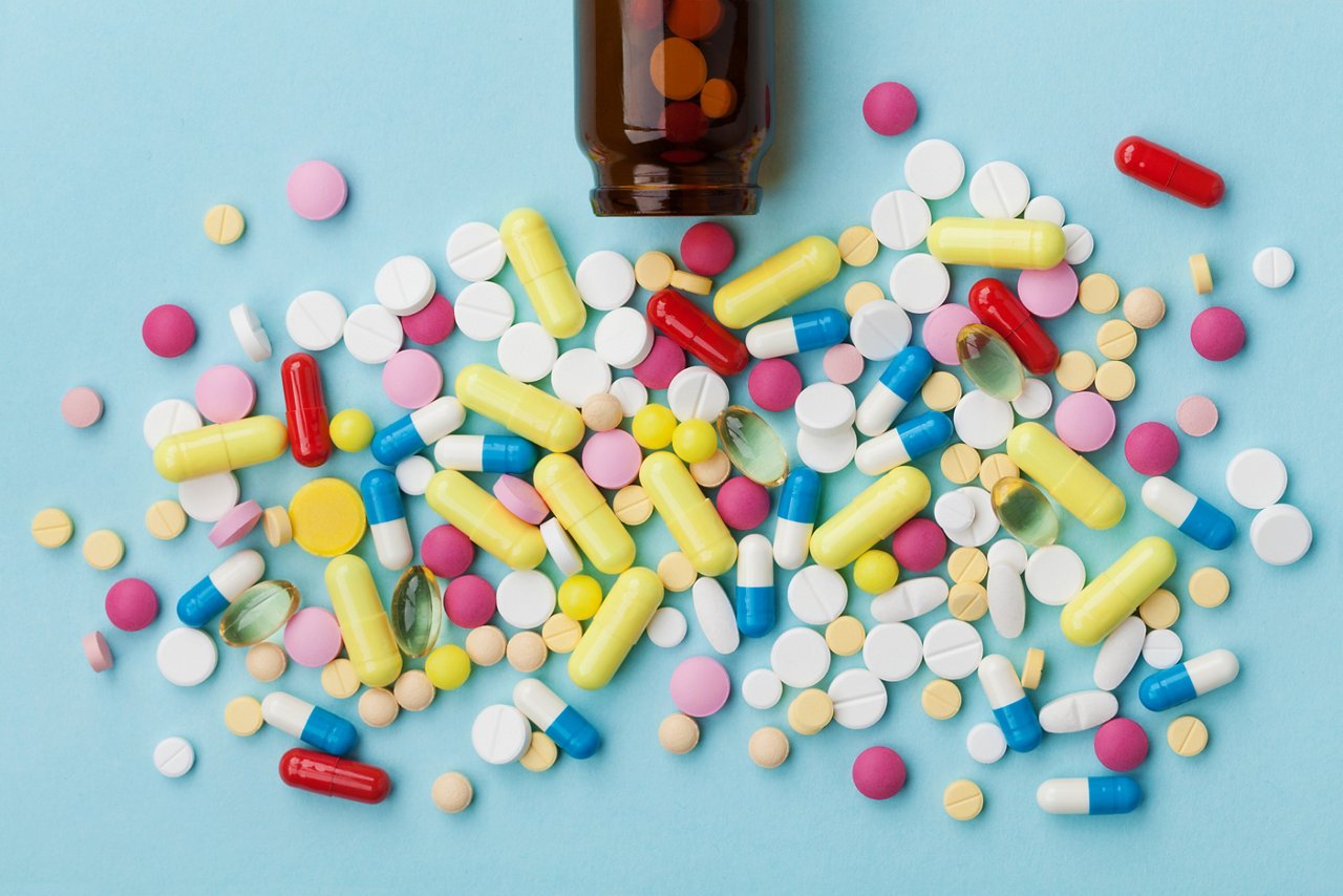 Viele bunte, ausgeschüttete Medikamentenpillen auf blauem Hintergrund, pharmazeutisches Konzept