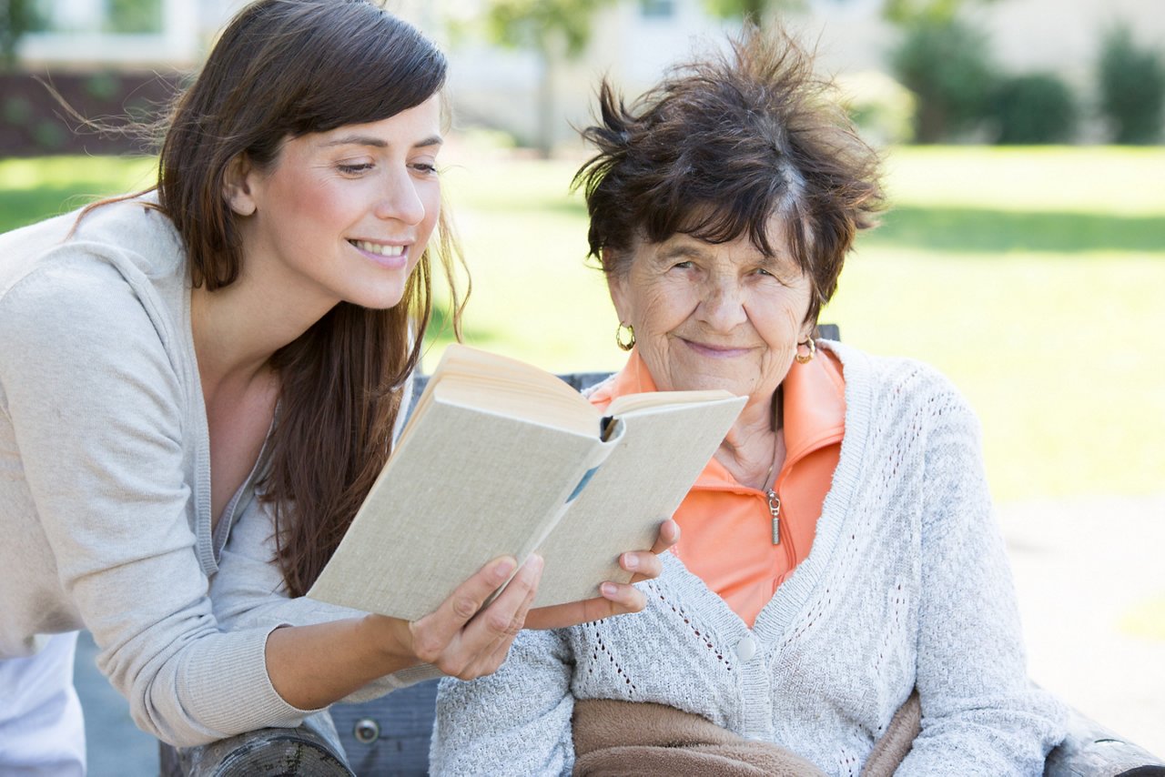 Junge Frau liest Seniorin ein Buch vor