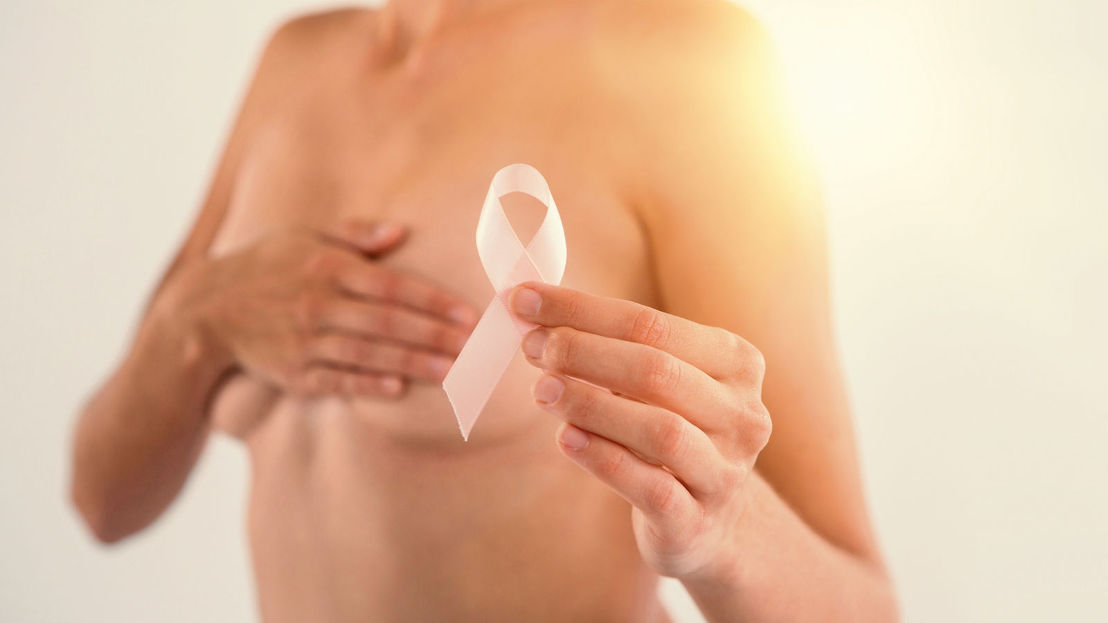 Mid section of topless woman holding pink ribbon