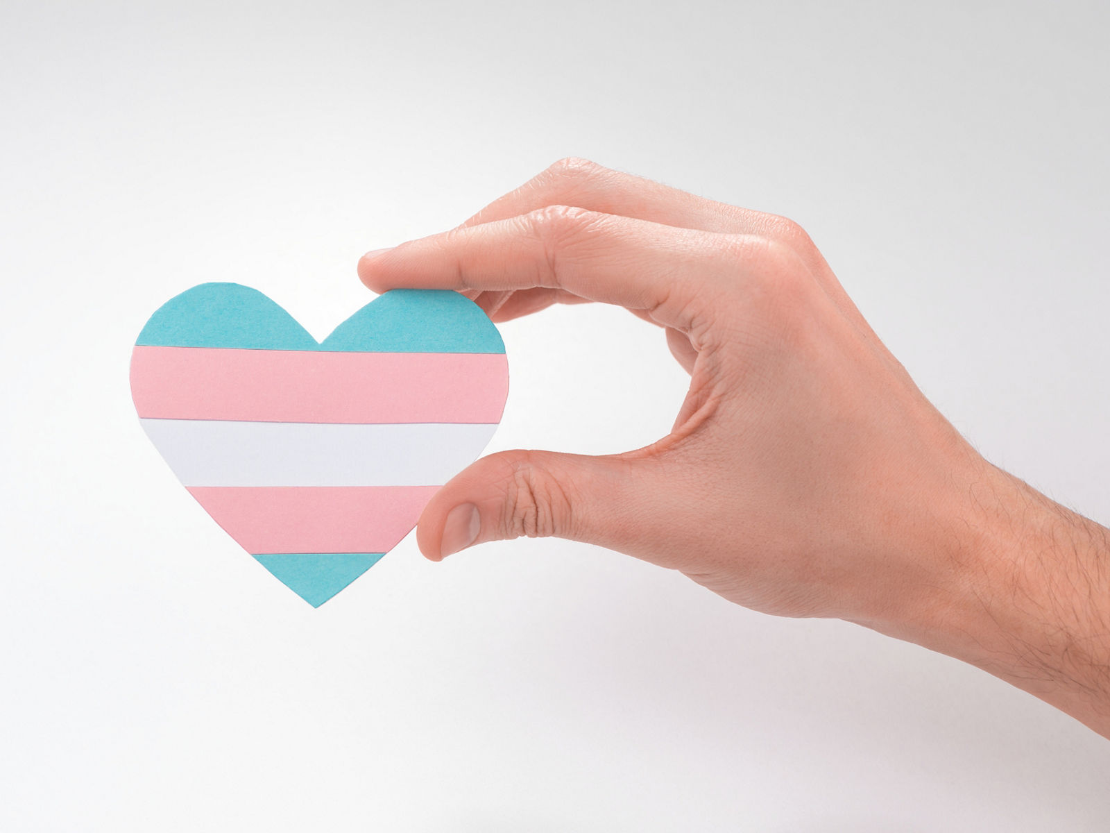 Hand holding a paper heart with transgender flag on white background. Beautiful art to express pride of trans people.