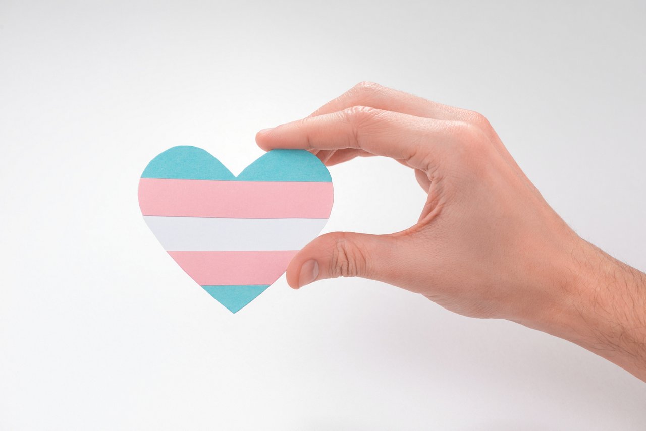Hand holding a paper heart with transgender flag on white background. Beautiful art to express pride of trans people.