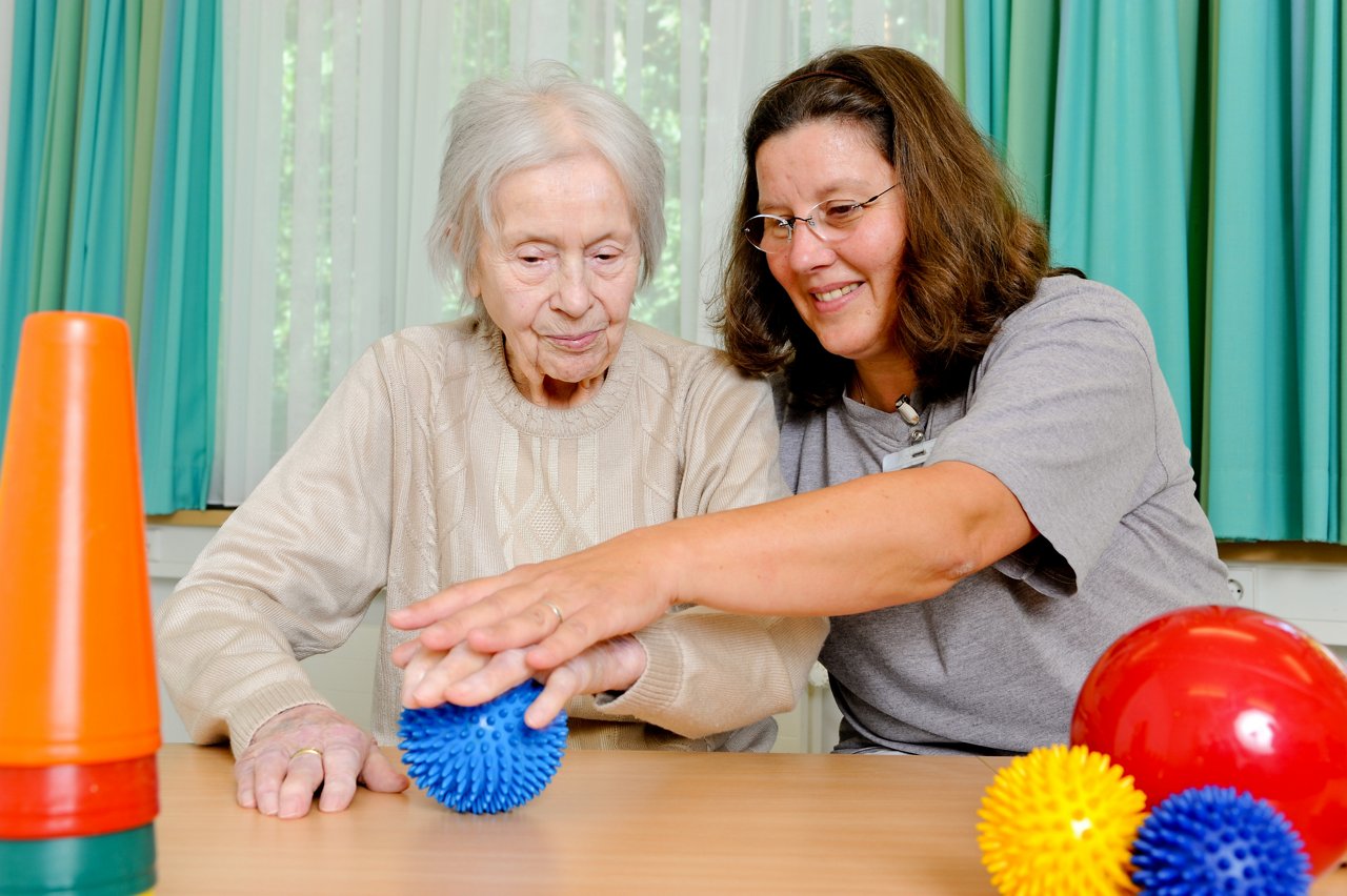 Physiotherapeutin und Geriatrie-Patientin üben Mobilisierung am Ball