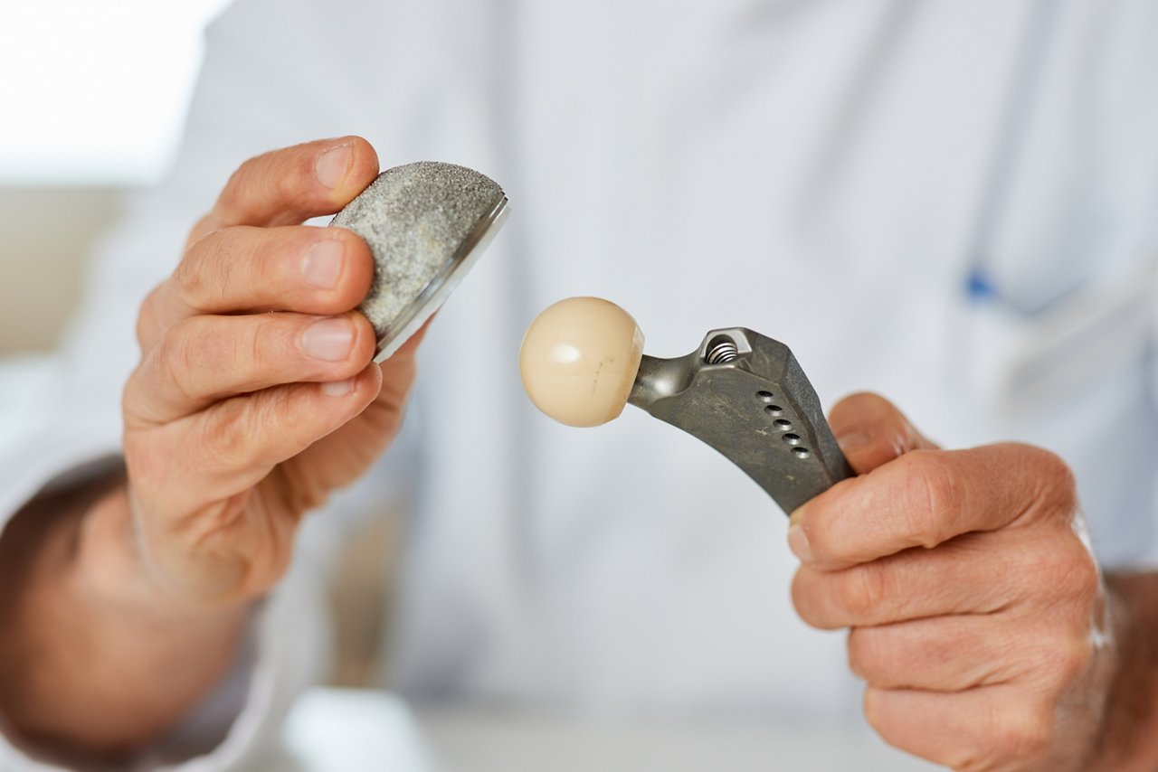 Arzt zeigt in seinen Händen künstliches Hüftgelenk, Kugelgelenk