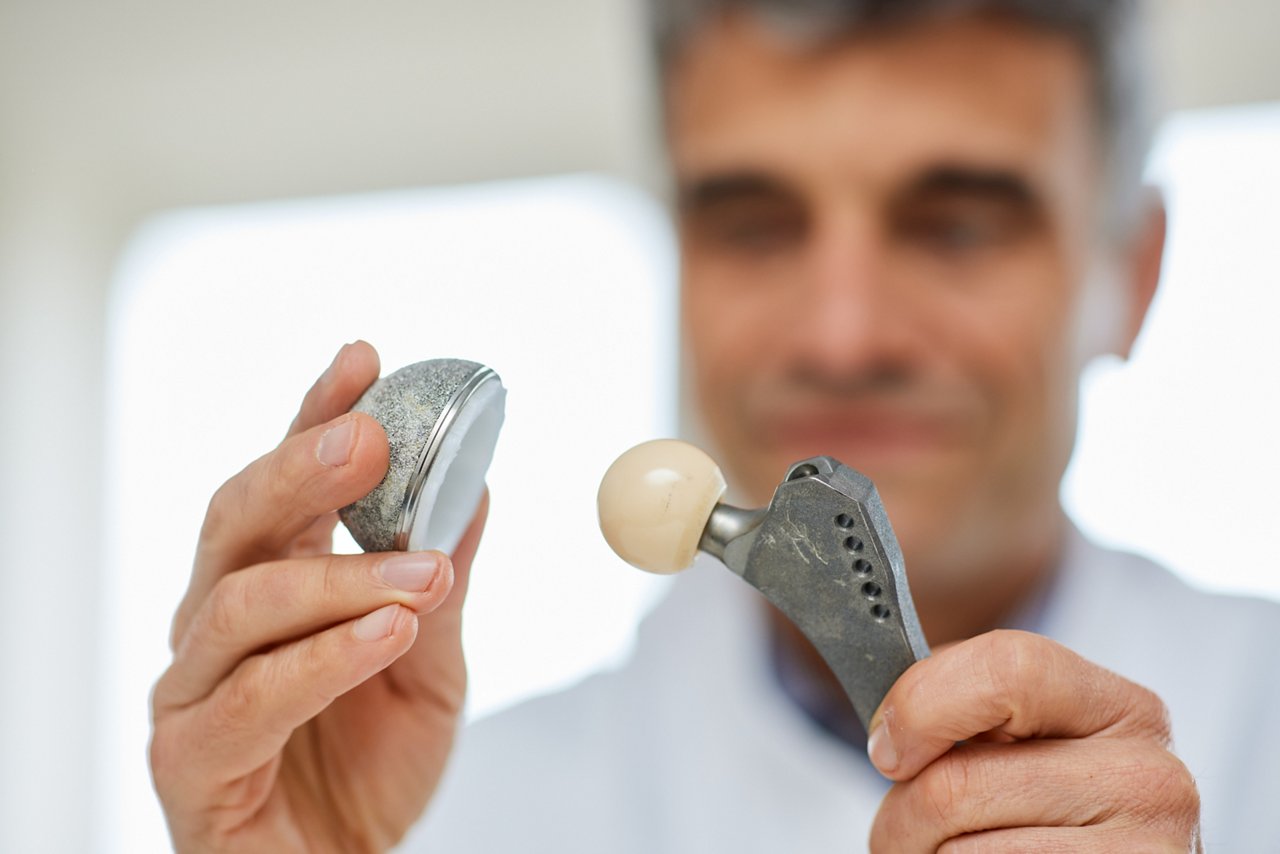 Arzt zeigt in seinen Händen künstliches Hüftgelenk, Kugelgelenk