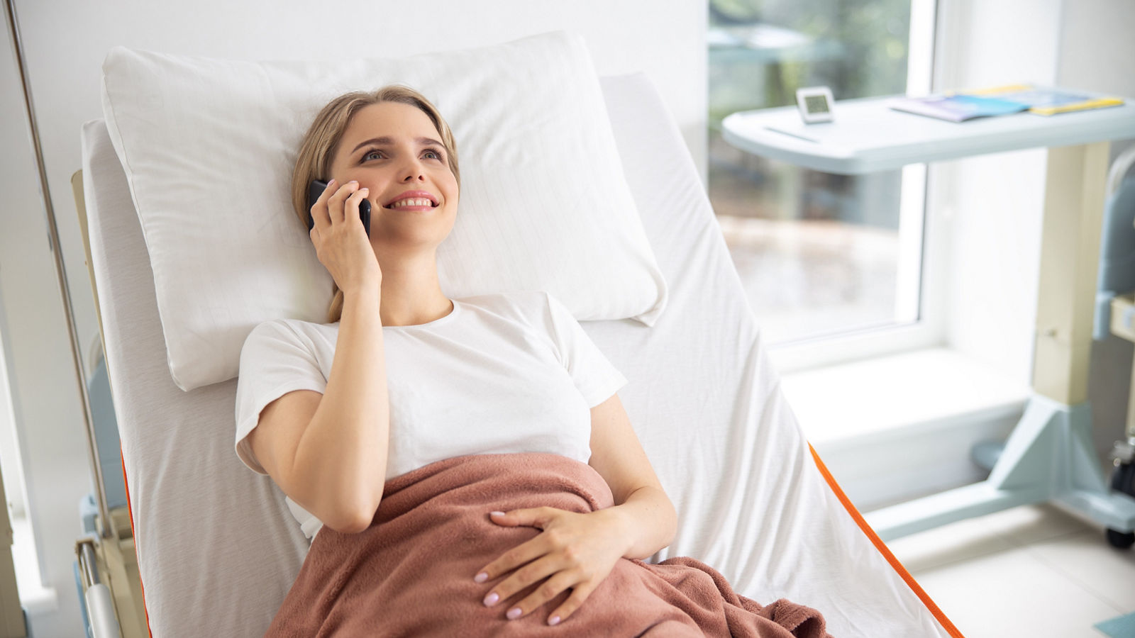 Smiling lady having phone conversation in hospital room