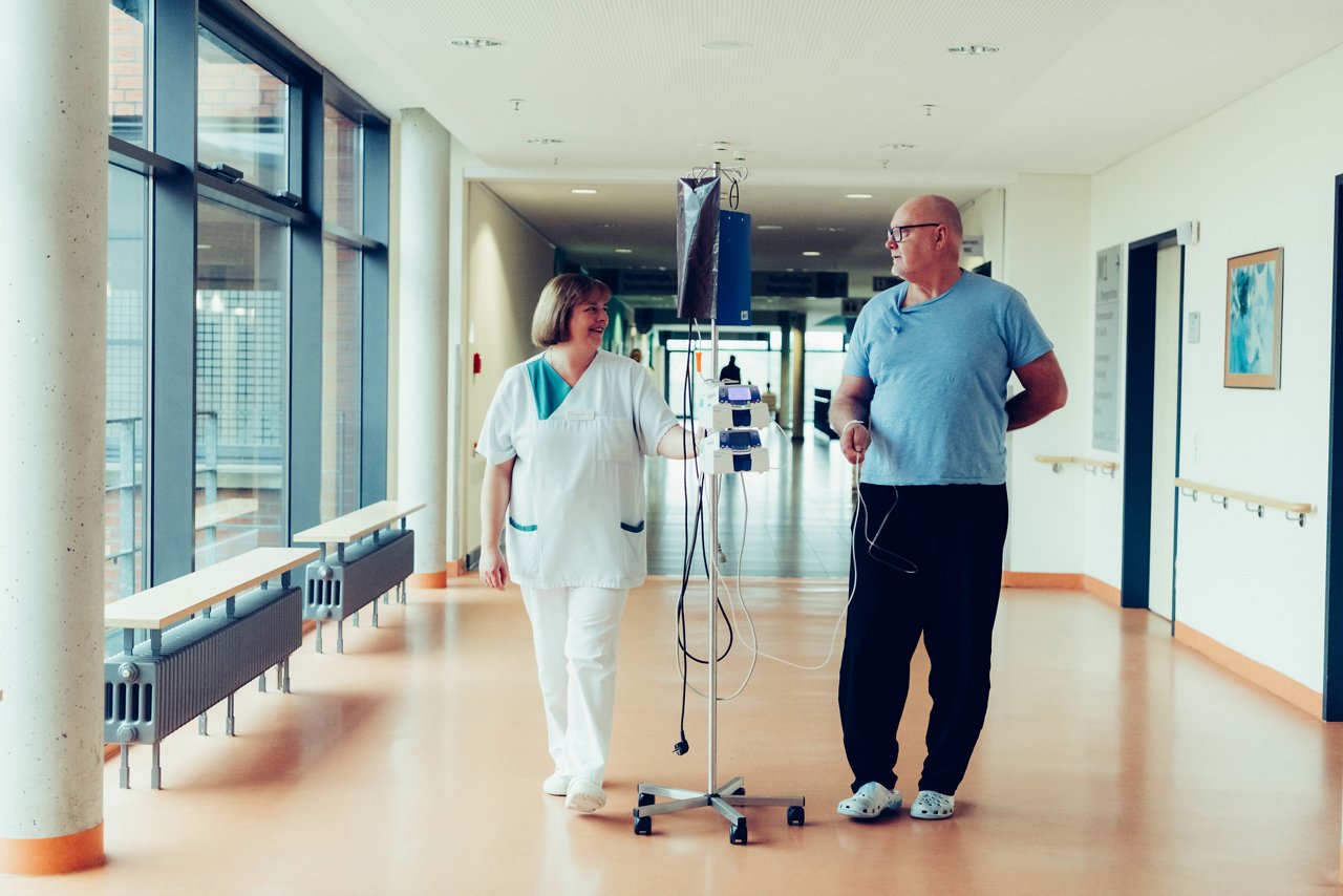 Pflegerin und Patient mit Infusionsständer im Gespräch auf dem Flur