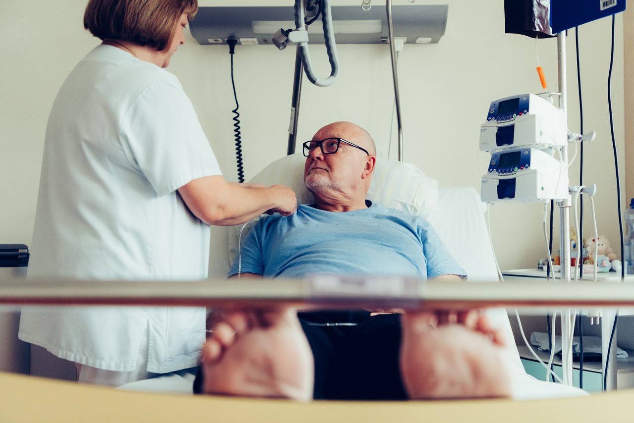 Pflegerin legt Patient im Krankenbett einen Infusionsschlauch für die Chemotherapie