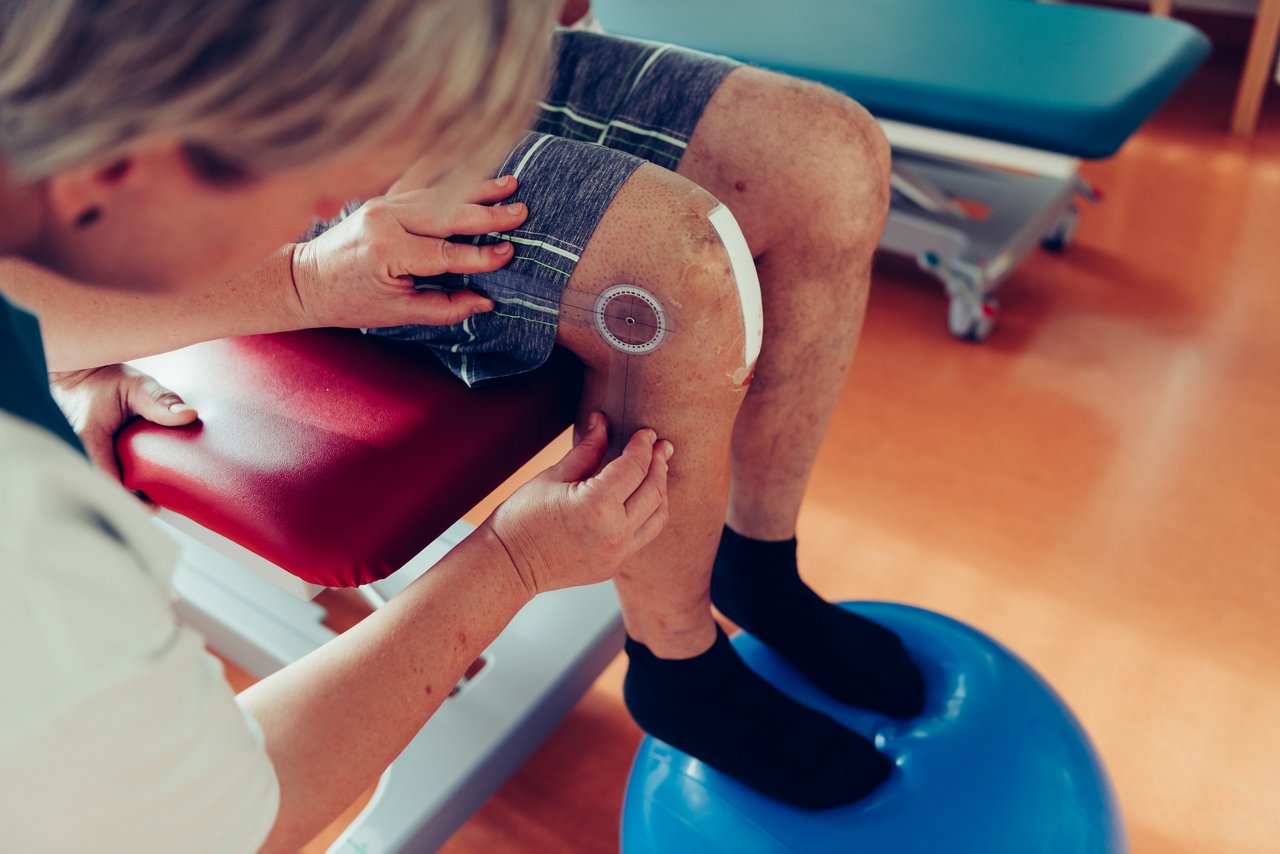 Physiotherapeutin nutzt ein Winkelmesser zum Ausmessen des Knies eines Patienten
